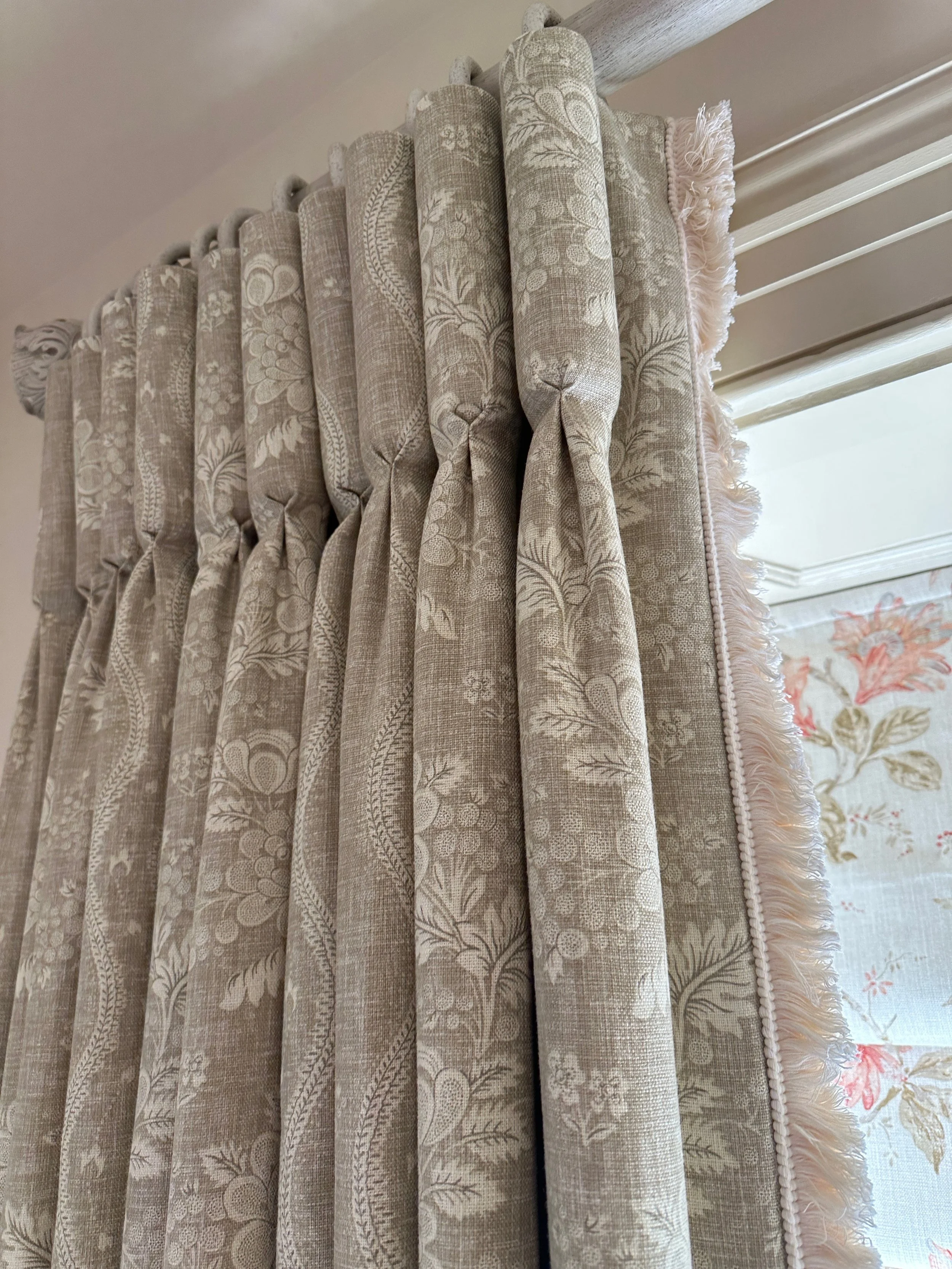 Close-up of beige patterned curtains with floral and vine design hanging over a window.
