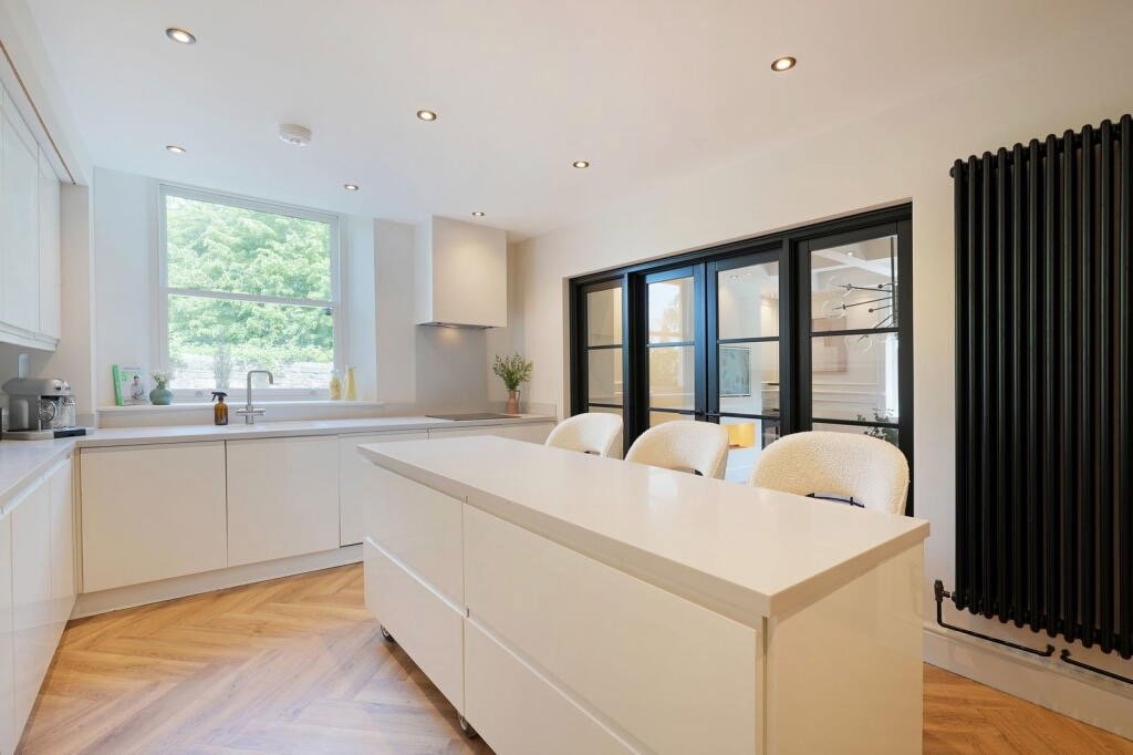 Modern kitchen with white cabinets, a white island, a window above the sink, black sliding glass doors, and wooden flooring.