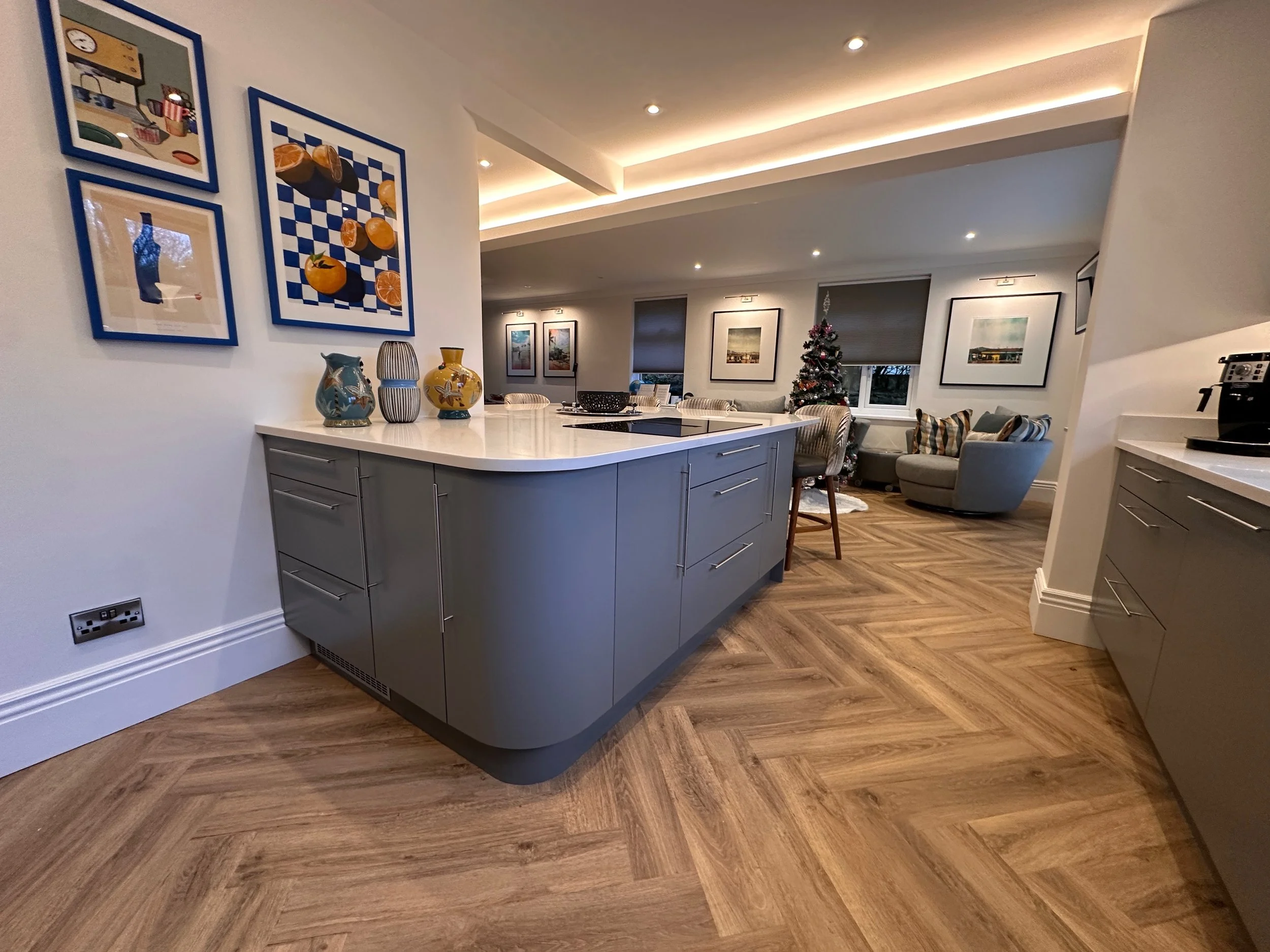 Modern open-plan kitchen with a grey island, decorated with colorful vases, and a living area with framed artwork, a Christmas tree, and comfortable seating.