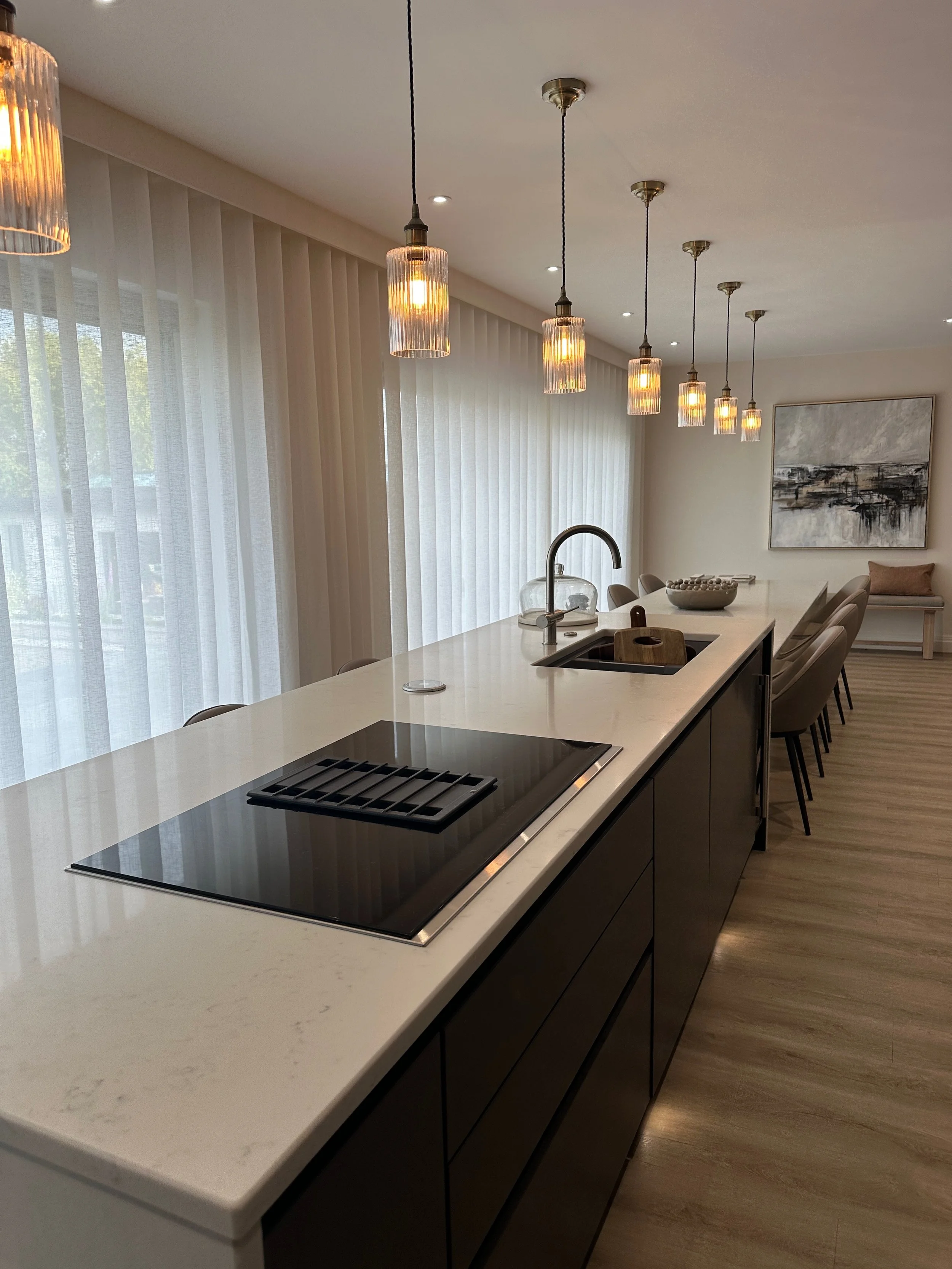 Modern kitchen with white marble island, black stove, and pendant lights, overlooking large windows with sheer curtains.
