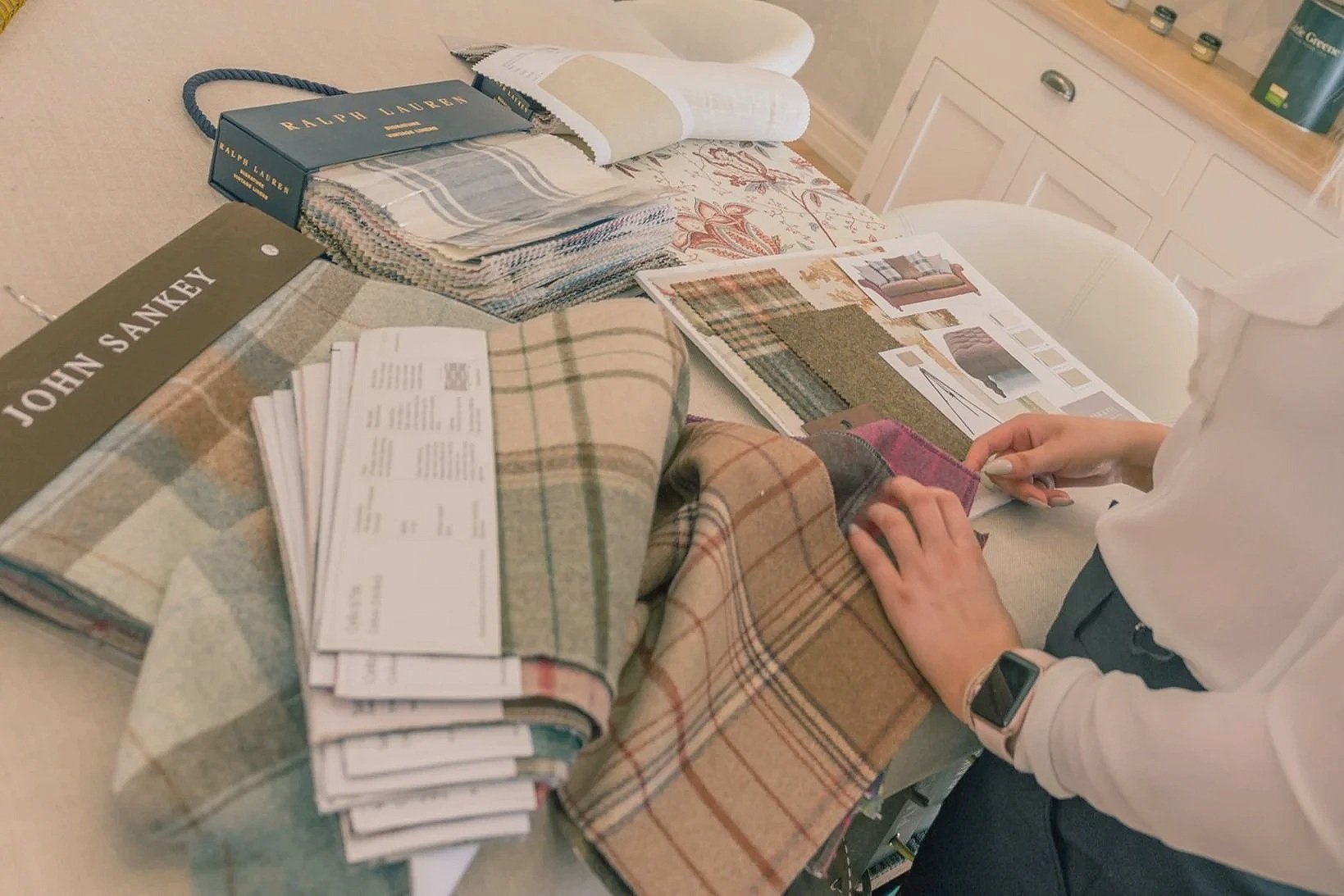 Person sitting at a table reviewing fabric swatches and interior design magazines with colour palettes and furniture samples. Sheffield based interior designers