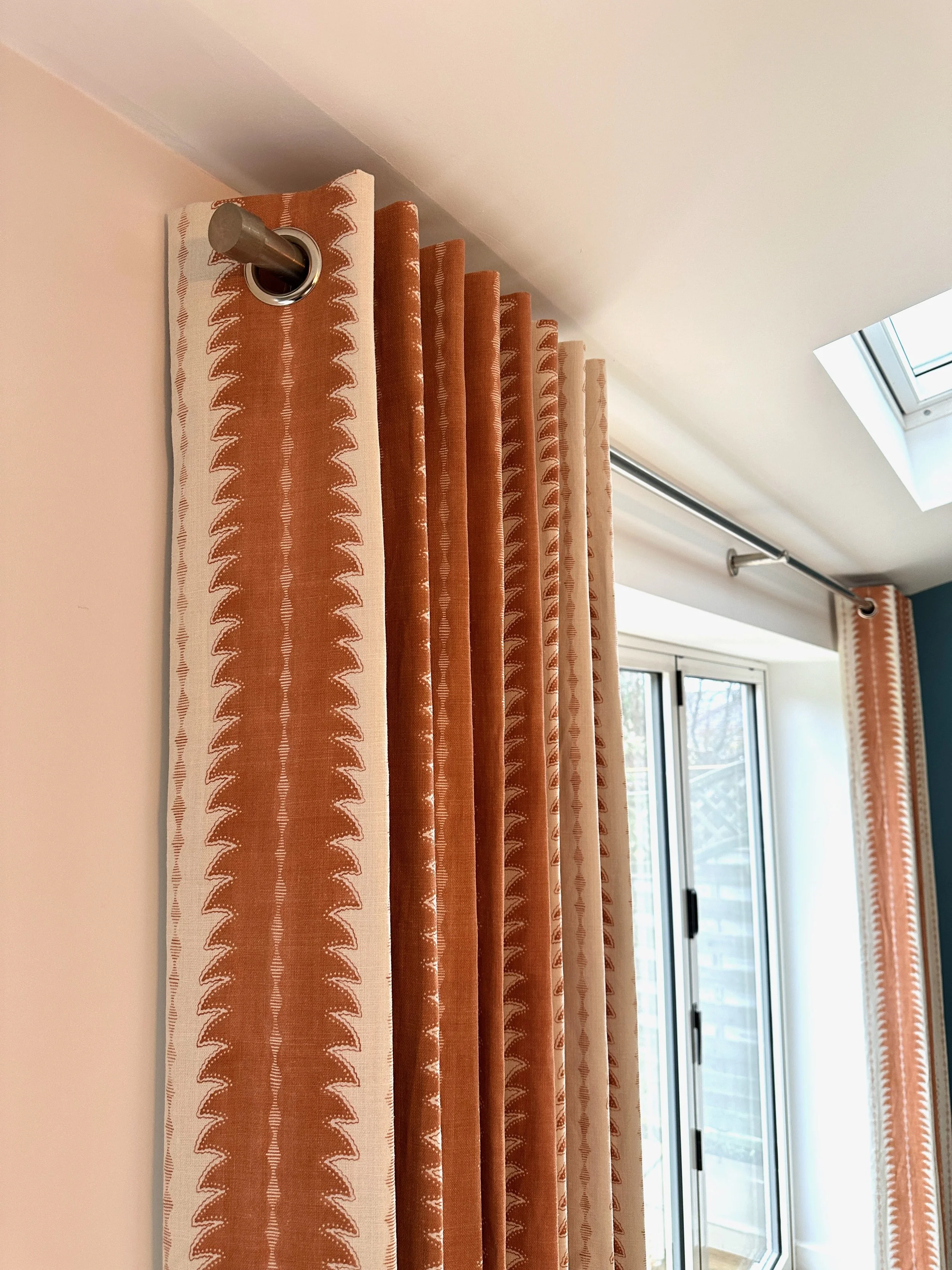 Close-up view of brown and cream patterned curtains hanging from a metal curtain rod above a sliding glass door, with a skylight window visible on the ceiling.