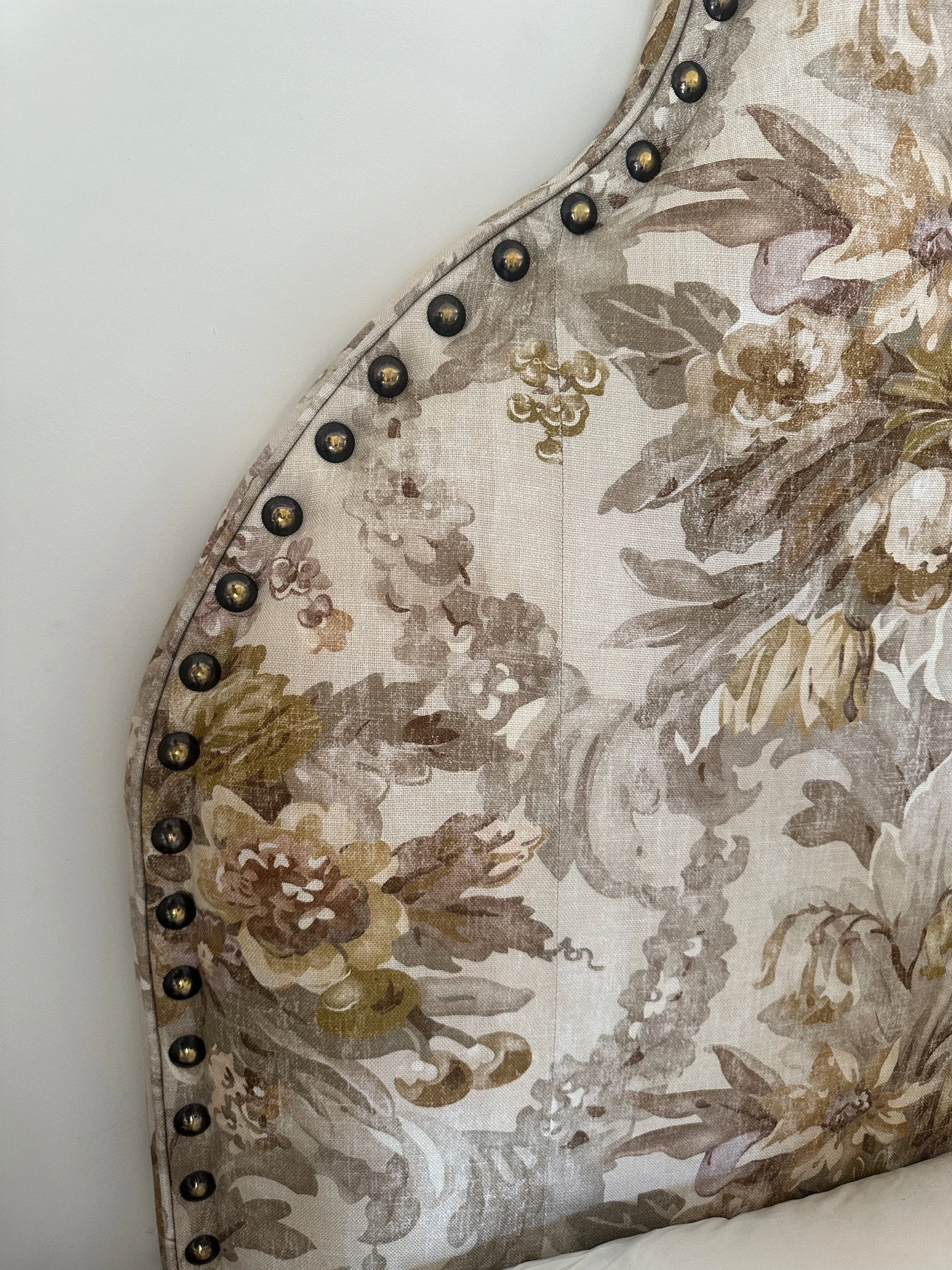 Close-up of a floral-patterned upholstered headboard with decorative nailhead trim.