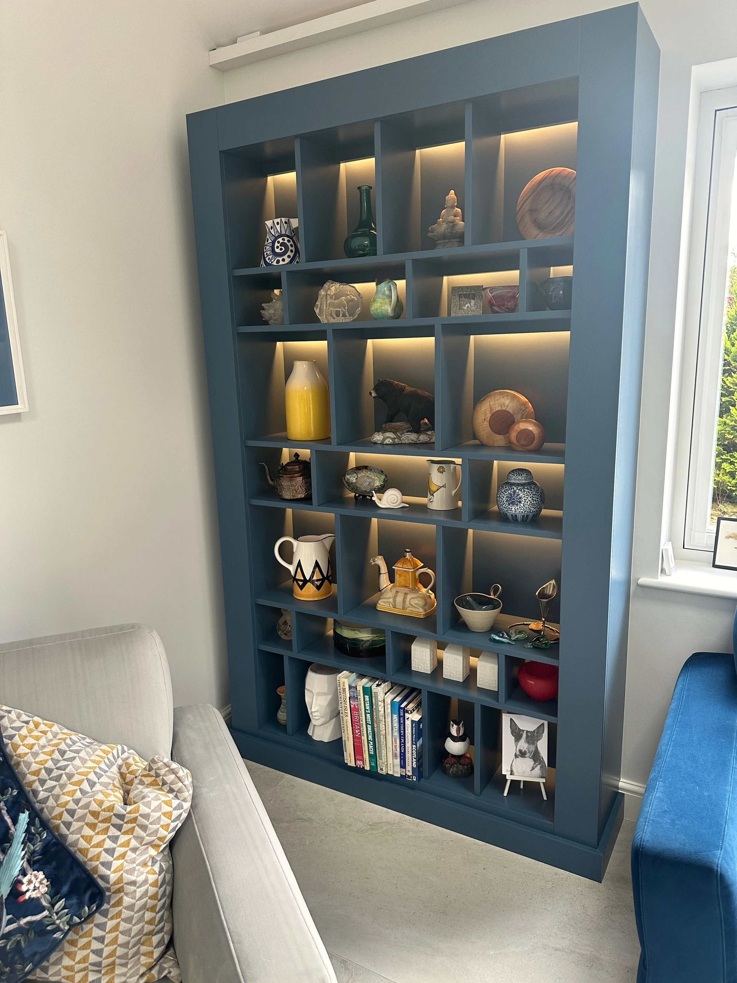 A blue bookshelf filled with various decorative items, including vases, sculptures, and books, positioned next to a window in a living room setting.