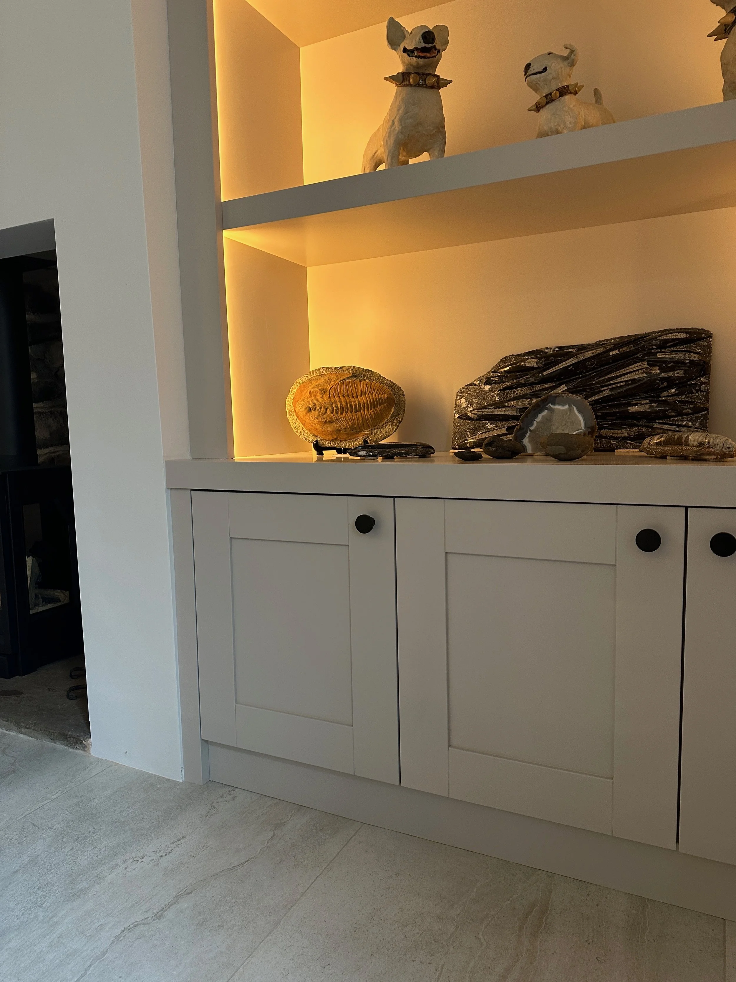 Built-in white cabinet with black knobs and decorative stones displayed on top, with two dog sculptures on the shelf above, illuminated with warm lighting.