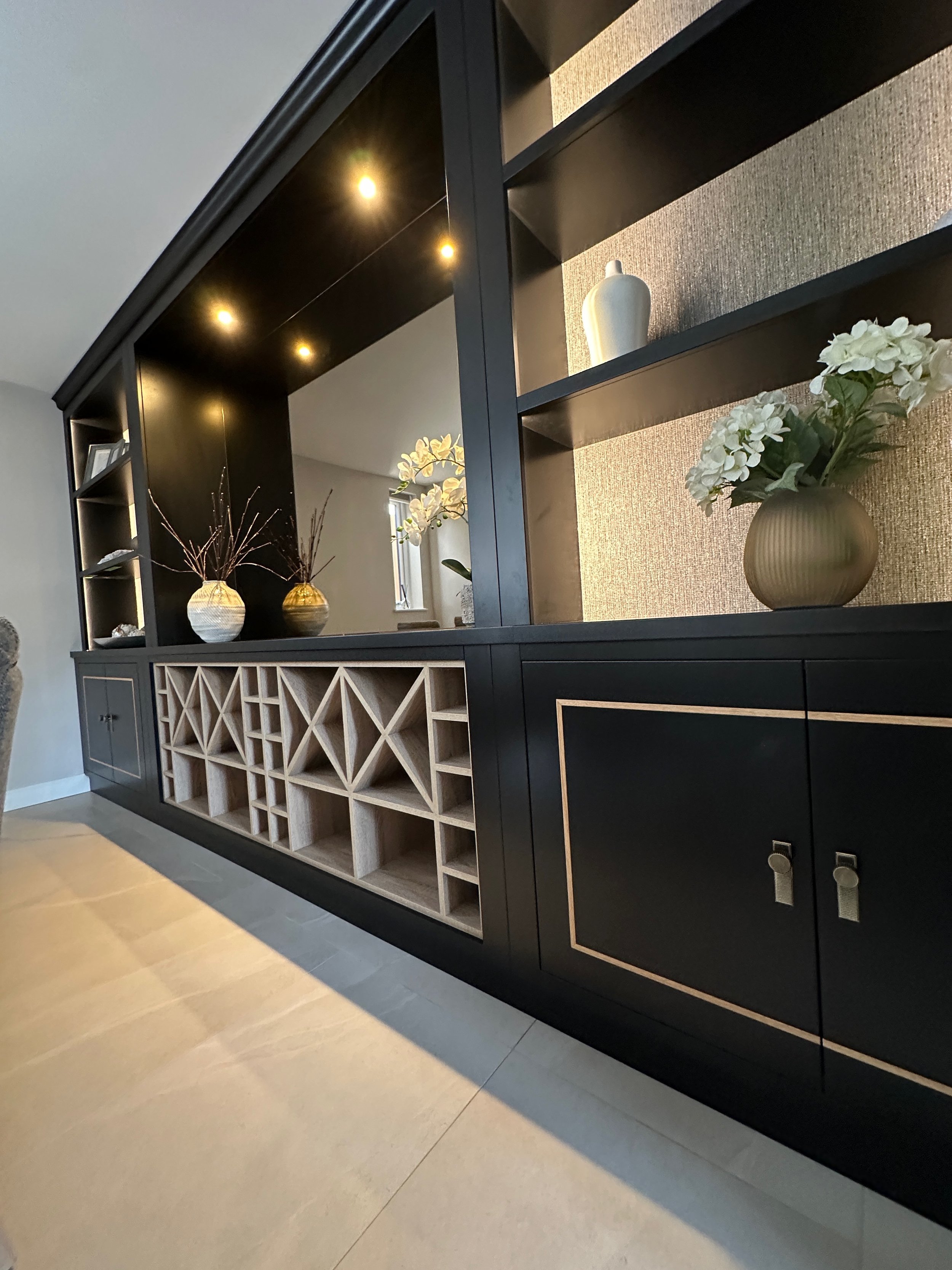 Black and beige modern shelving unit with decorative vases and flowers, and built-in wine rack on a beige tiled floor.