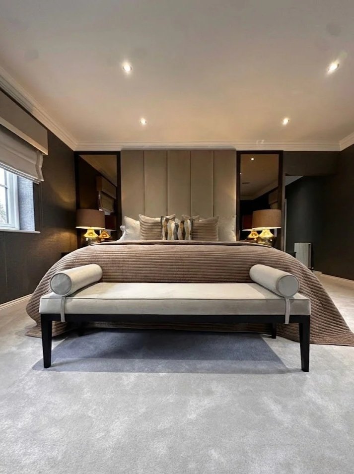 Modern bedroom with a large bed, beige headboard, and dark walls, featuring bedside lamps and window on the left.