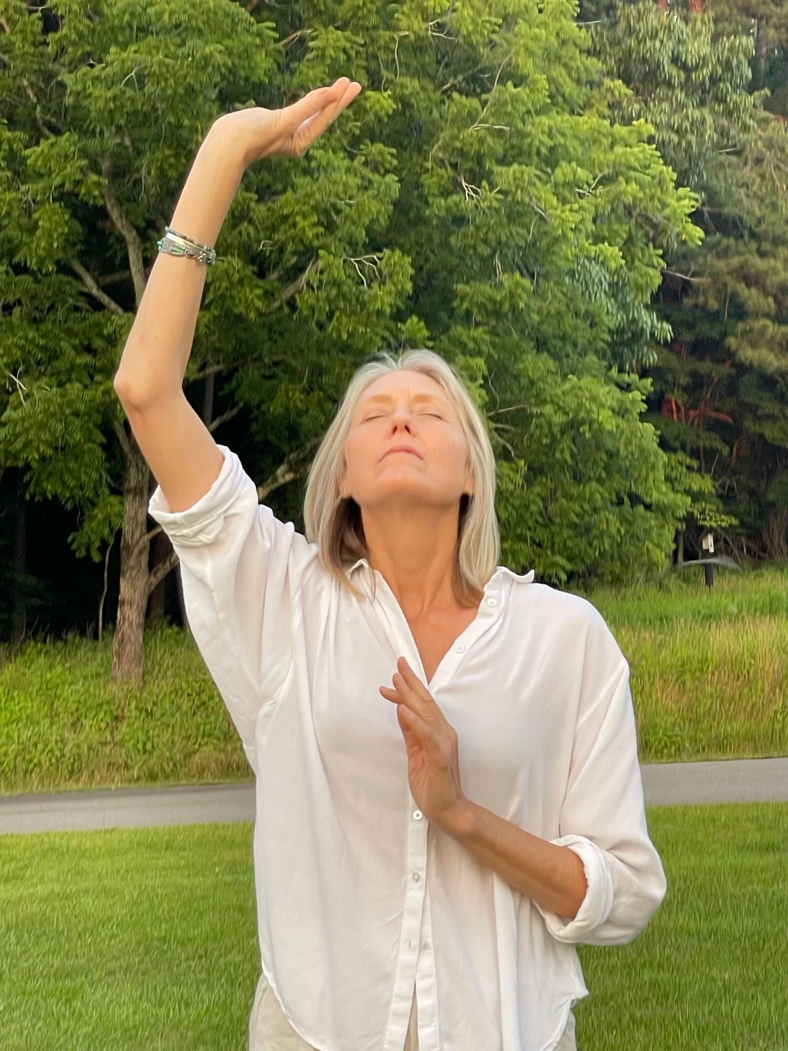 Woman with light hair in white shirt outdoors channeling with her hands through movement