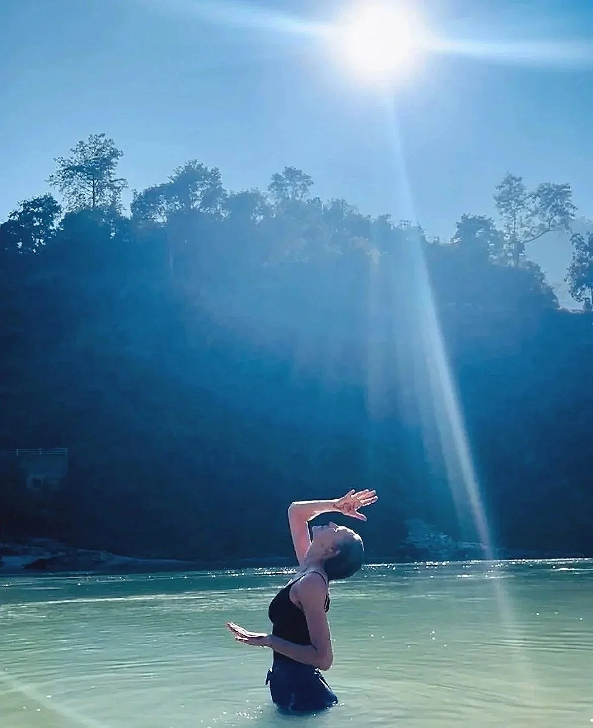 A woman standing in a body of water with sunlight above her head.