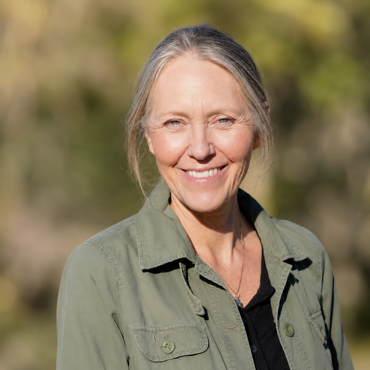 head and shoulders of woman with pulled back gray hair and blue eyes outdoors