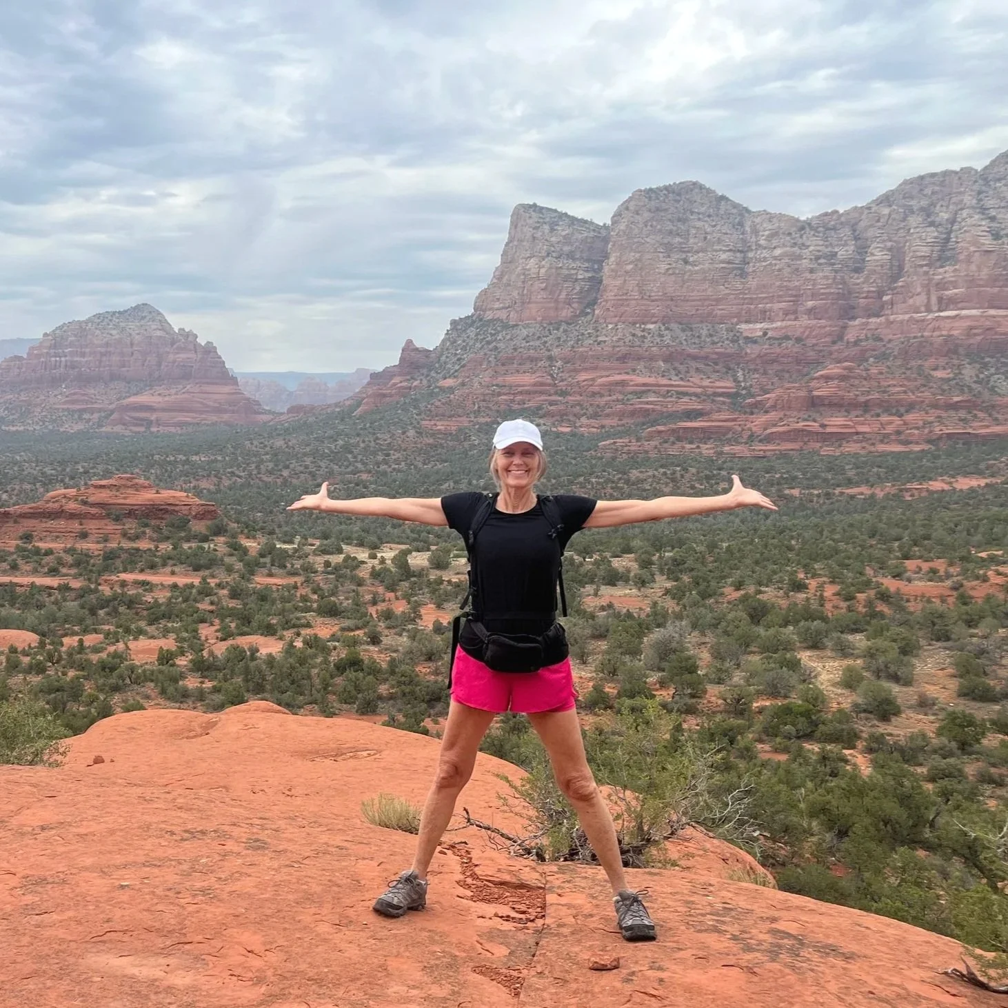 A woman standing on a red rock with mountains in background