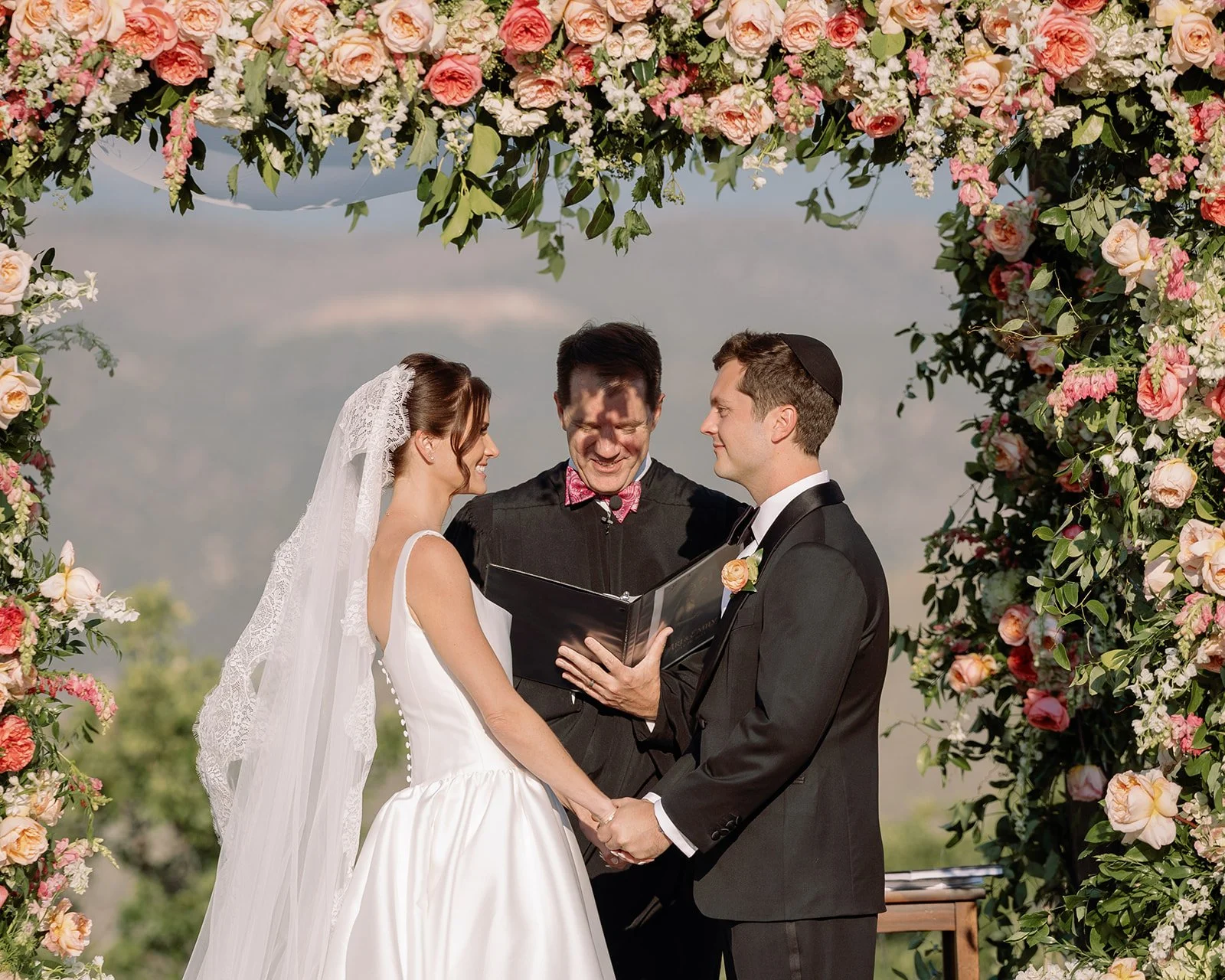 couple exchanging vows under floral bower archway