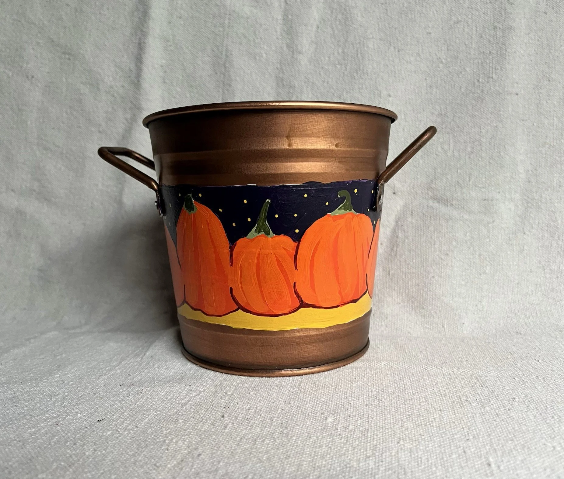 A hand painted pumpkin patch against a starry night sky, painted on a copper color tin bucket.