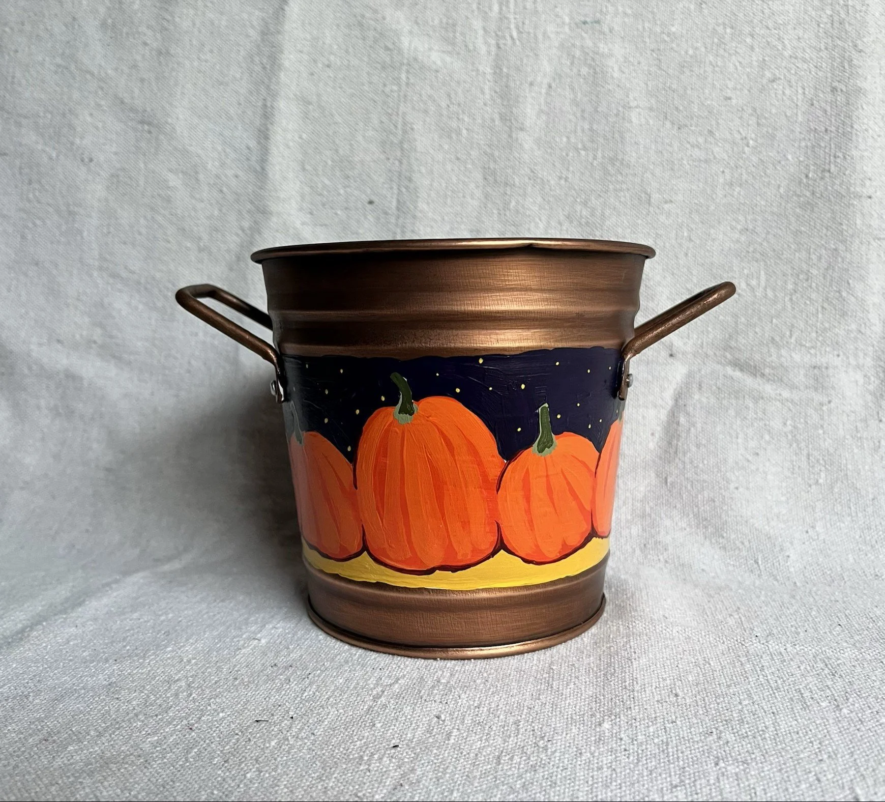 A hand painted pumpkin patch against a starry night sky, painted on a copper color tin bucket.