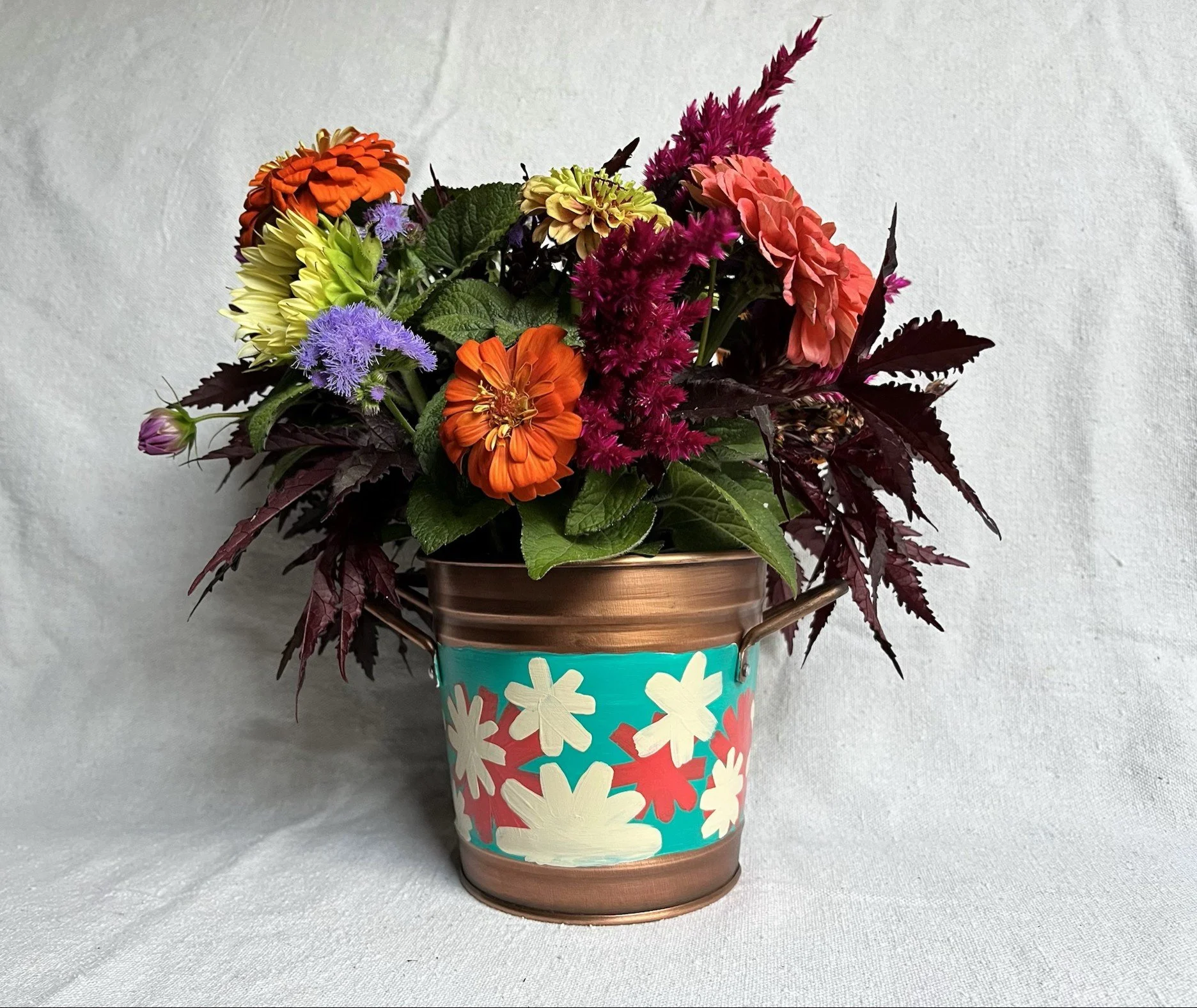 Copper color tin bucket with hand painted modern style flowers. Red, white and blue.