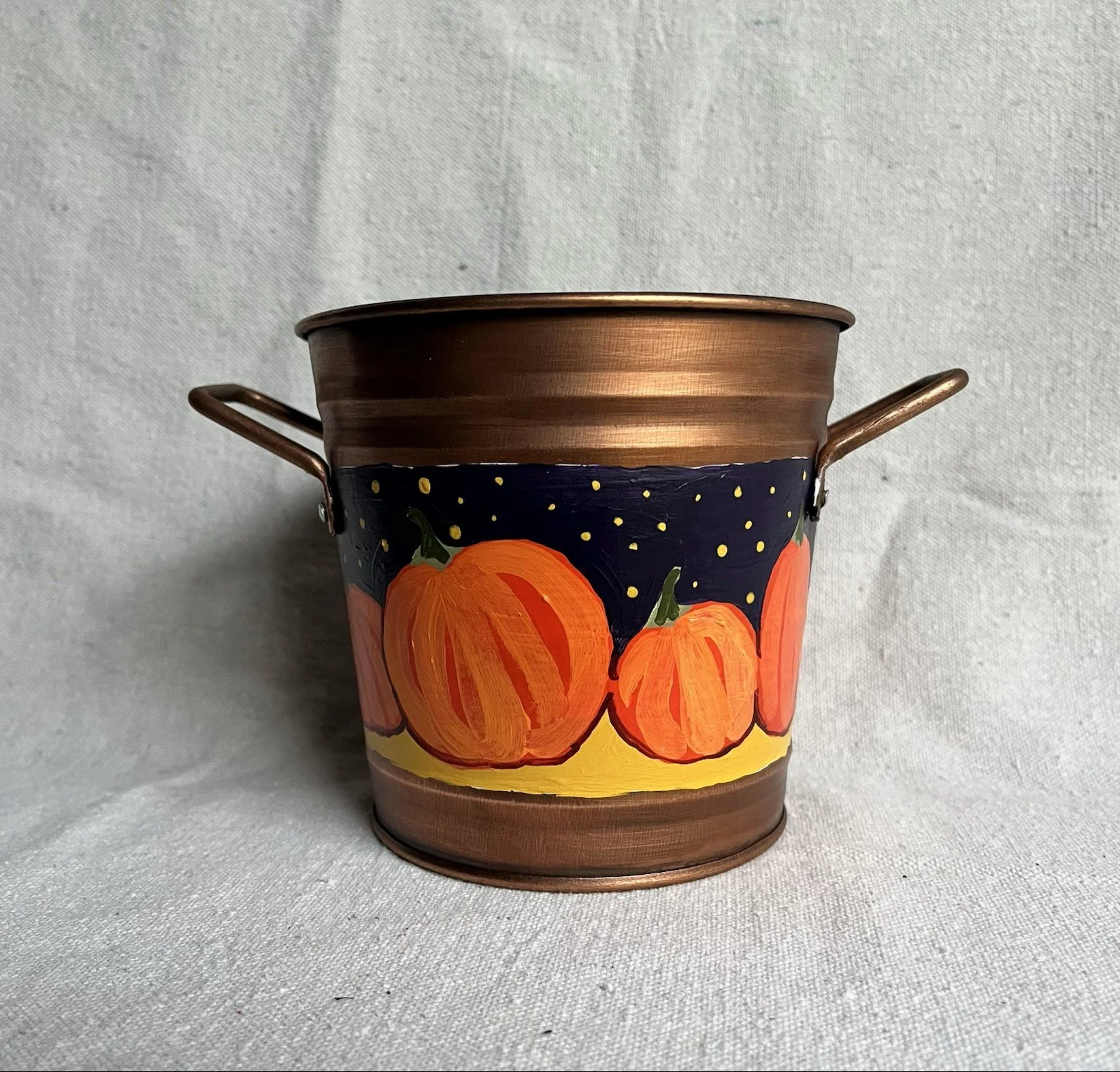 A hand painted pumpkin patch against a starry night sky, painted on a copper color tin bucket.