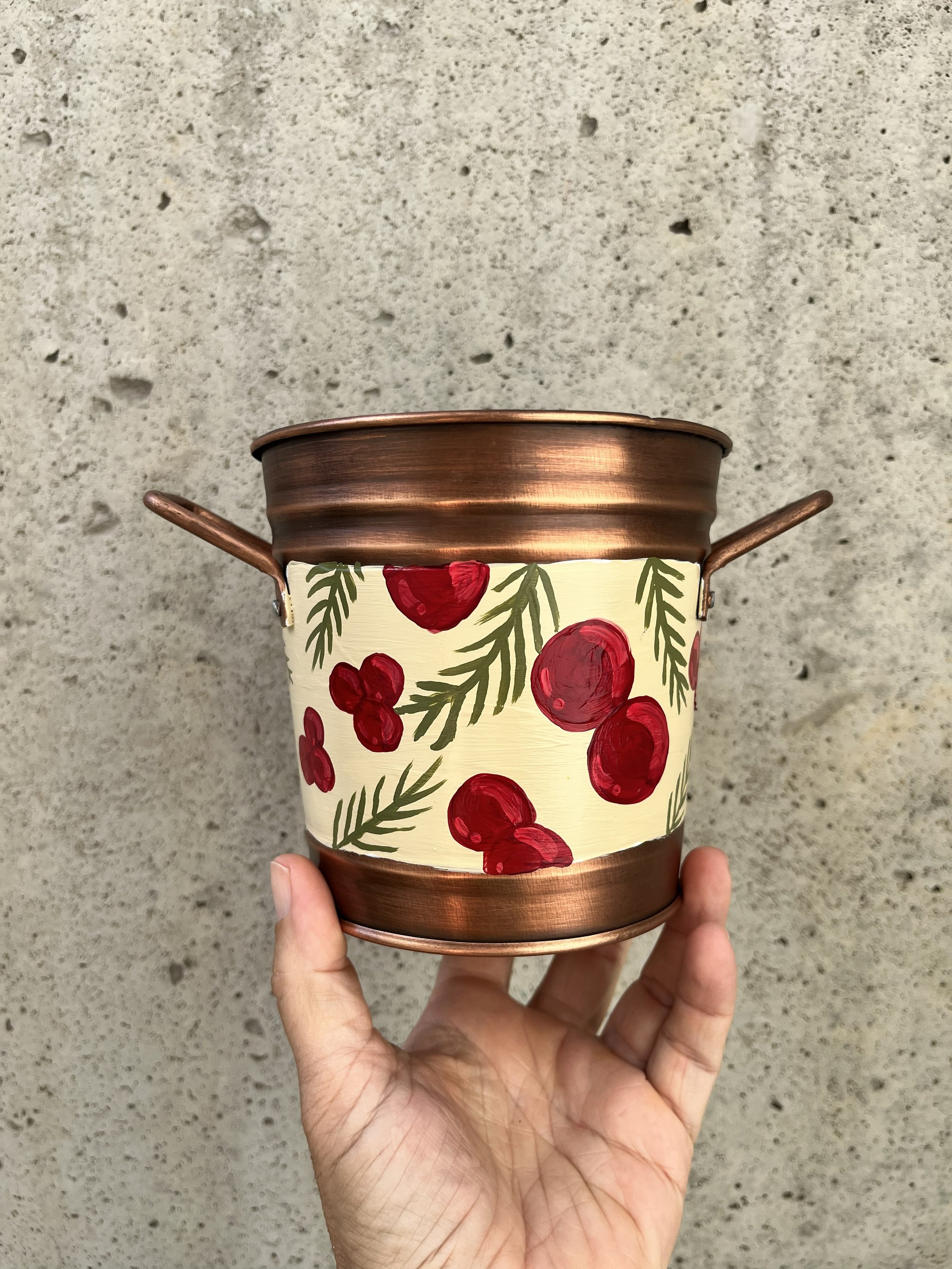 Hand painted decorative bucket. Red berries and sprigs of green herbs adorn this copper color bucket.