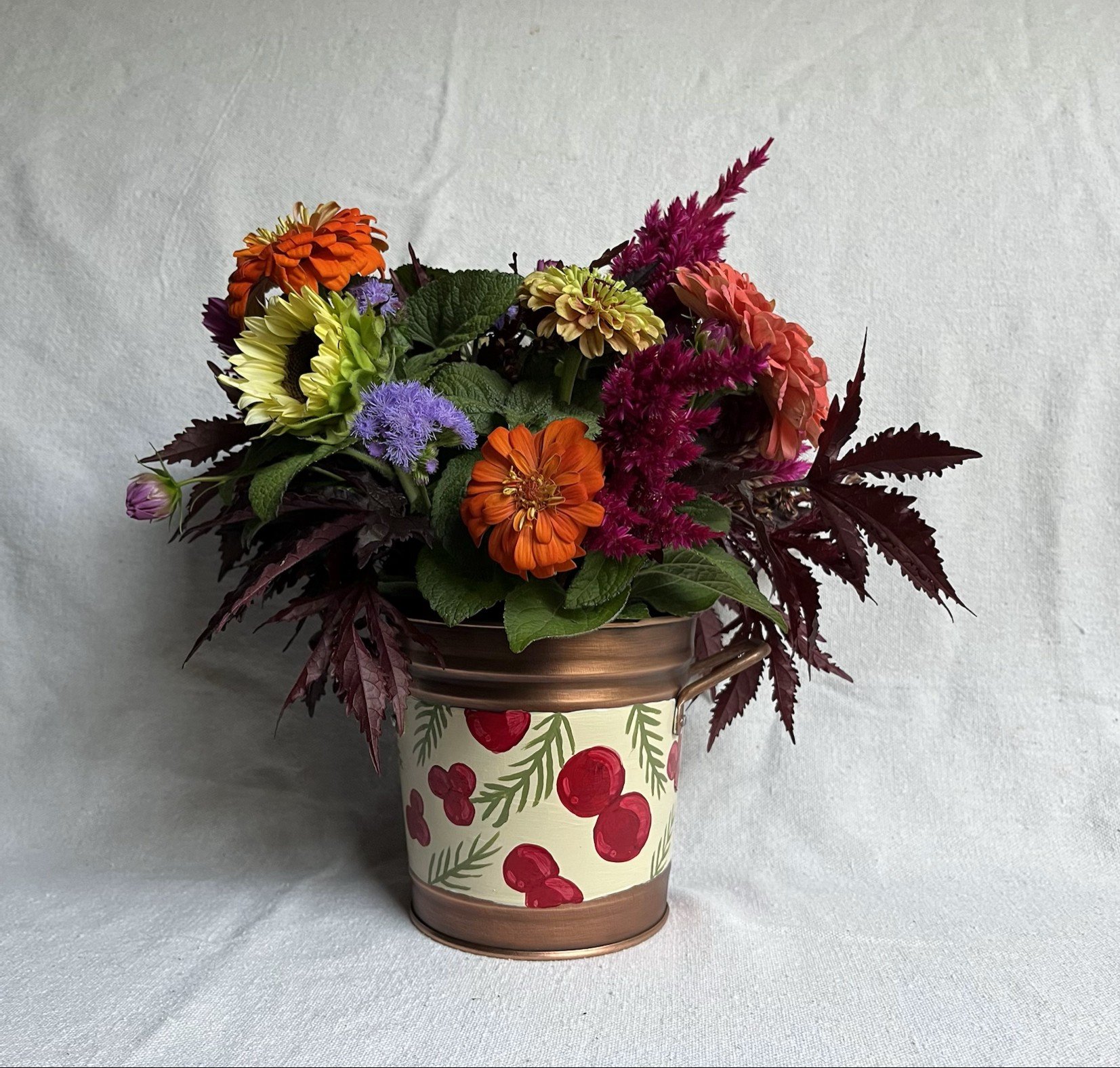 Hand painted decorative bucket. Red berries and sprigs of green herbs adorn this copper color bucket.