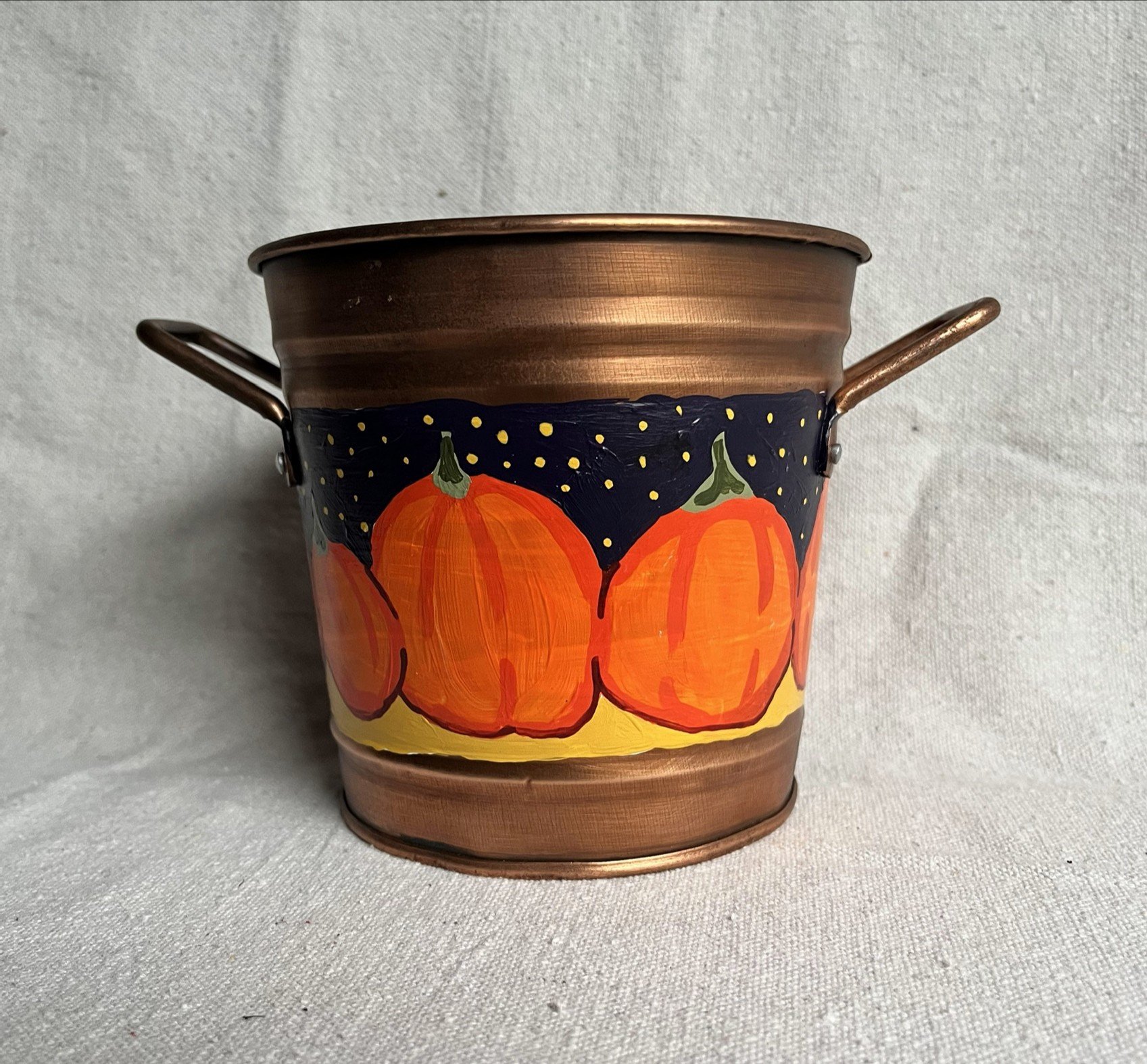A hand painted pumpkin patch against a starry night sky, painted on a copper color tin bucket.