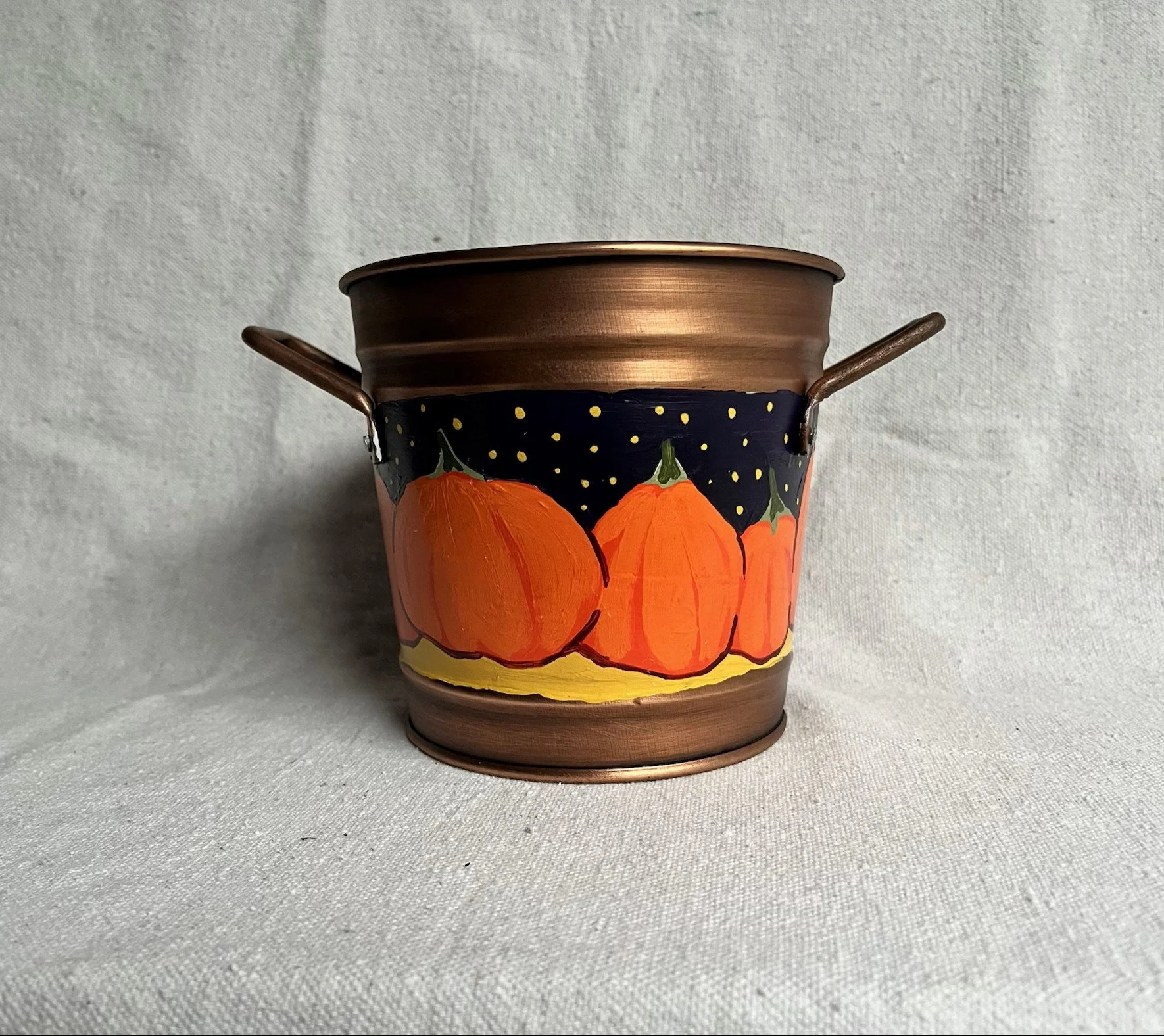 A hand painted pumpkin patch against a starry night sky, painted on a copper color tin bucket.