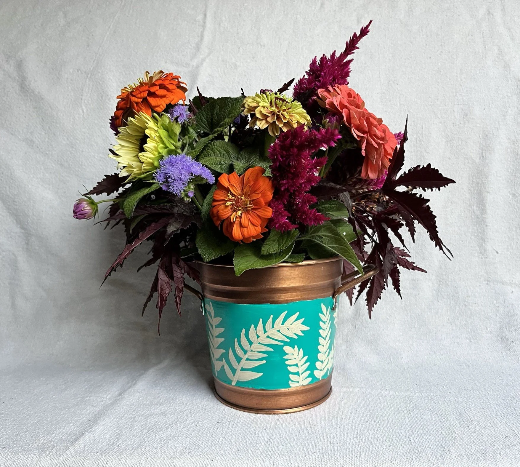 Hand painted frond of leaves on a blue background. Copper color bucket.
