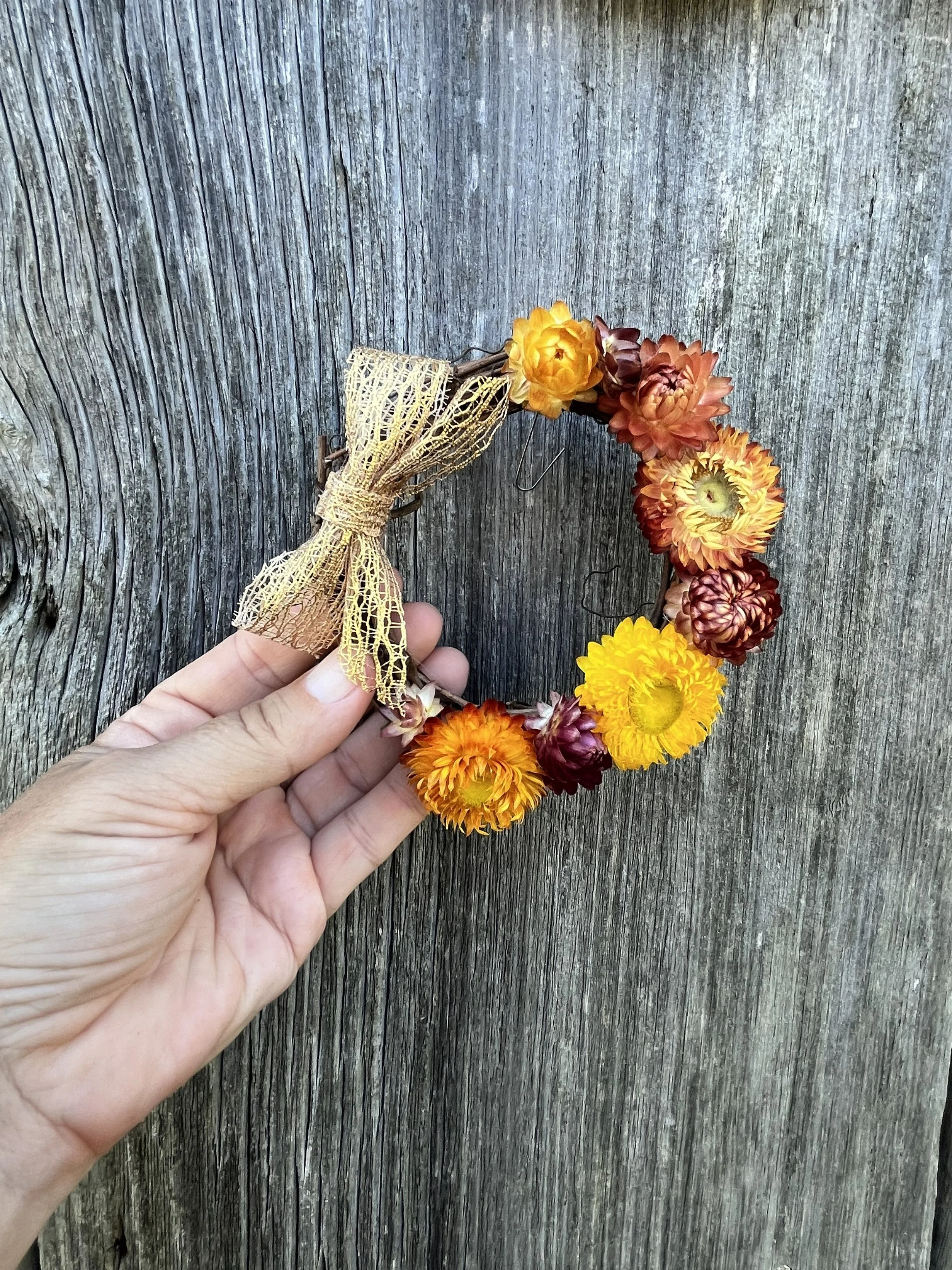 A miniature grapevine wreath affixed with a golden bow and dried strawflowers of varying colors.