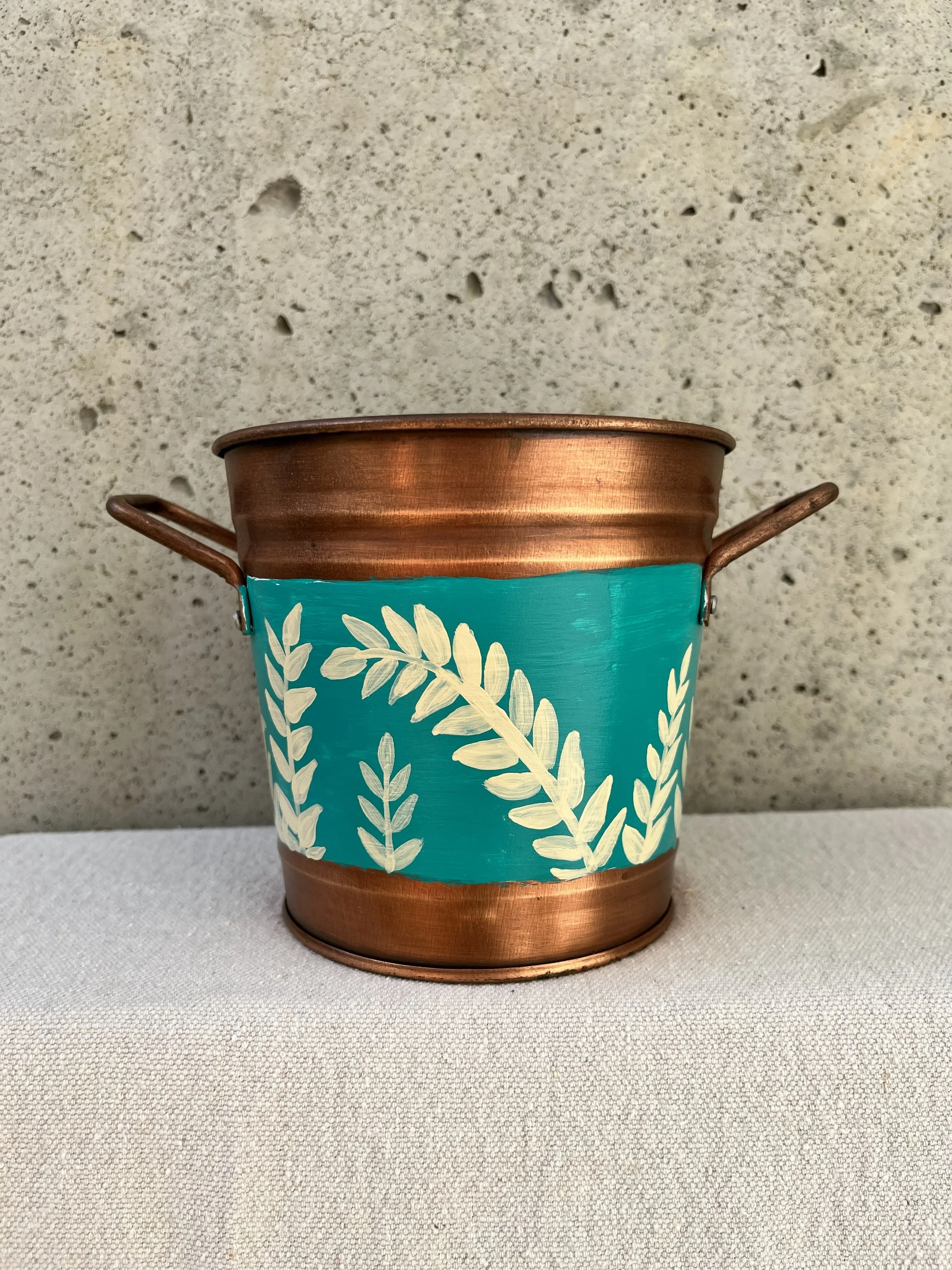 Hand painted frond of leaves on a blue background. Copper color bucket.