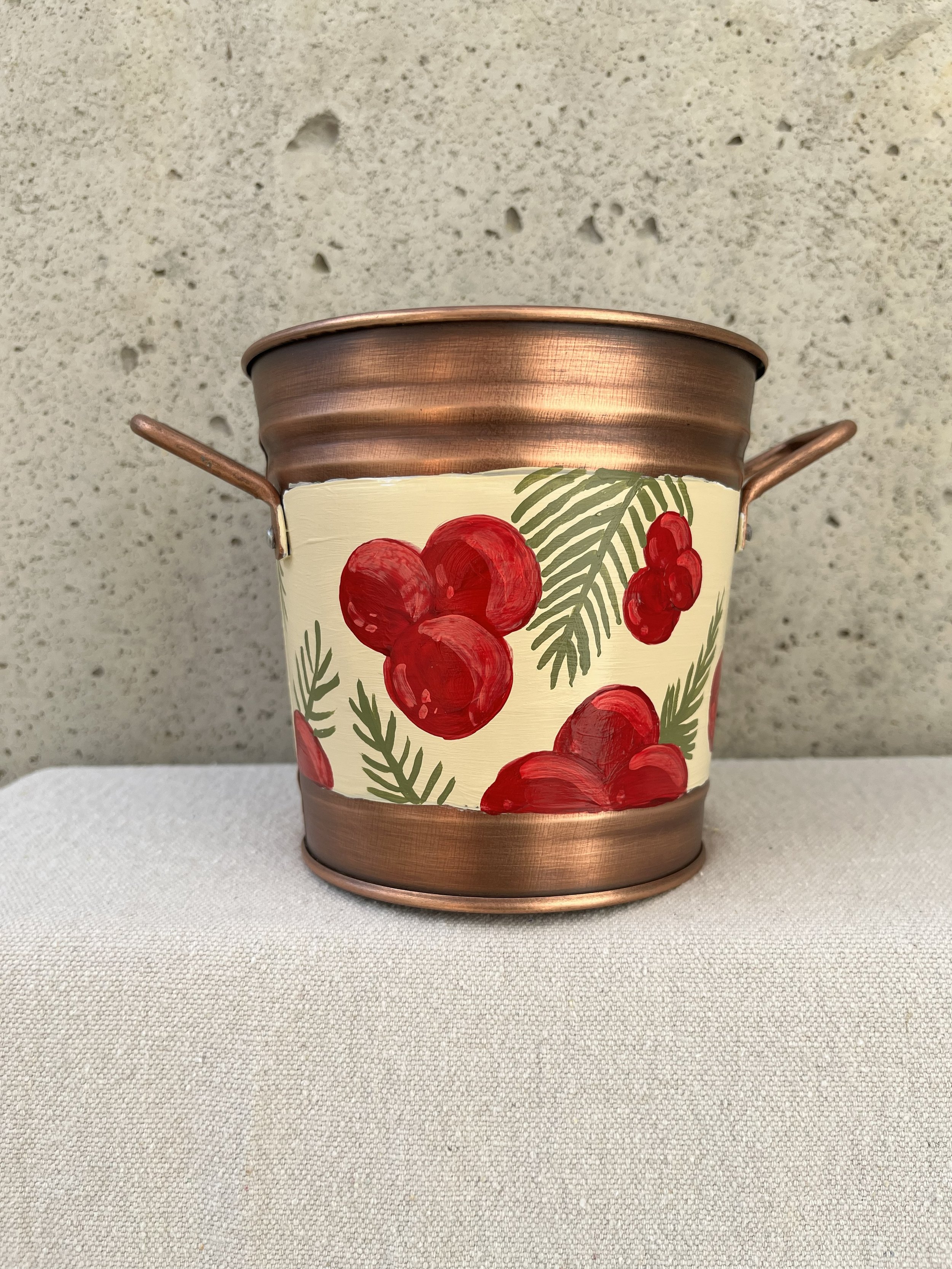 Hand painted decorative bucket. Red berries and sprigs of green herbs adorn this copper color bucket.