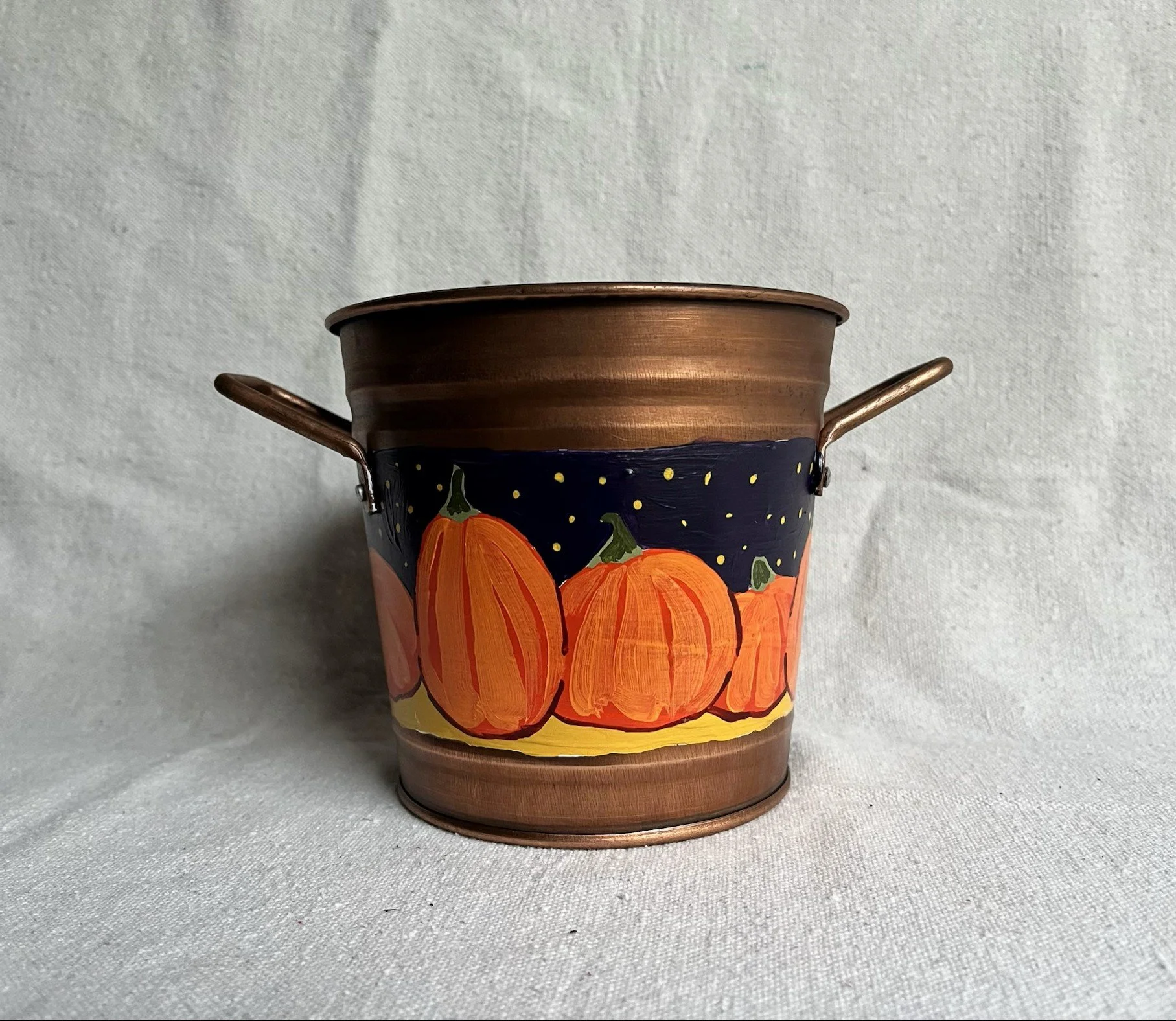 A hand painted pumpkin patch against a starry night sky, painted on a copper color tin bucket.