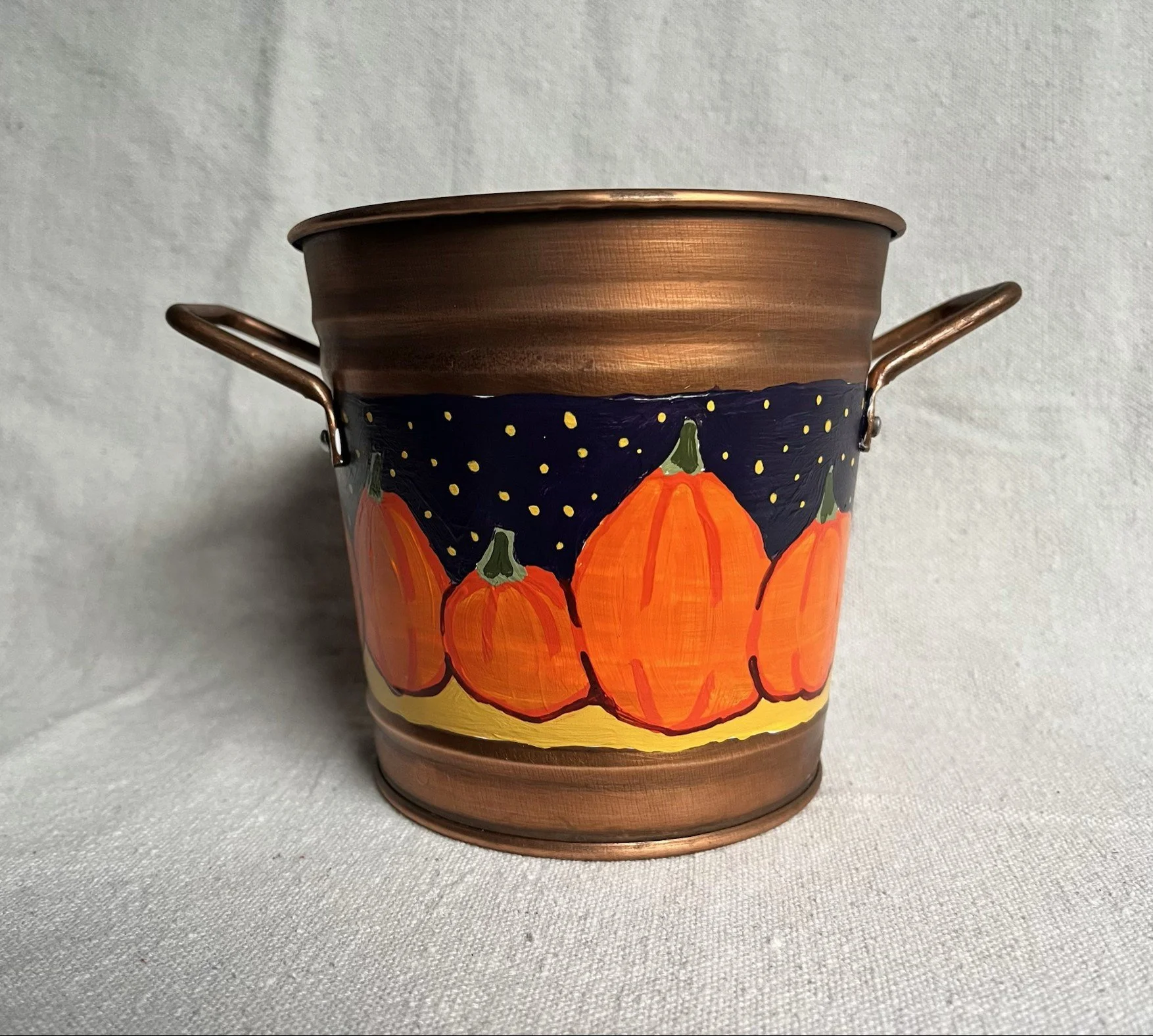 A hand painted pumpkin patch against a starry night sky, painted on a copper color tin bucket.