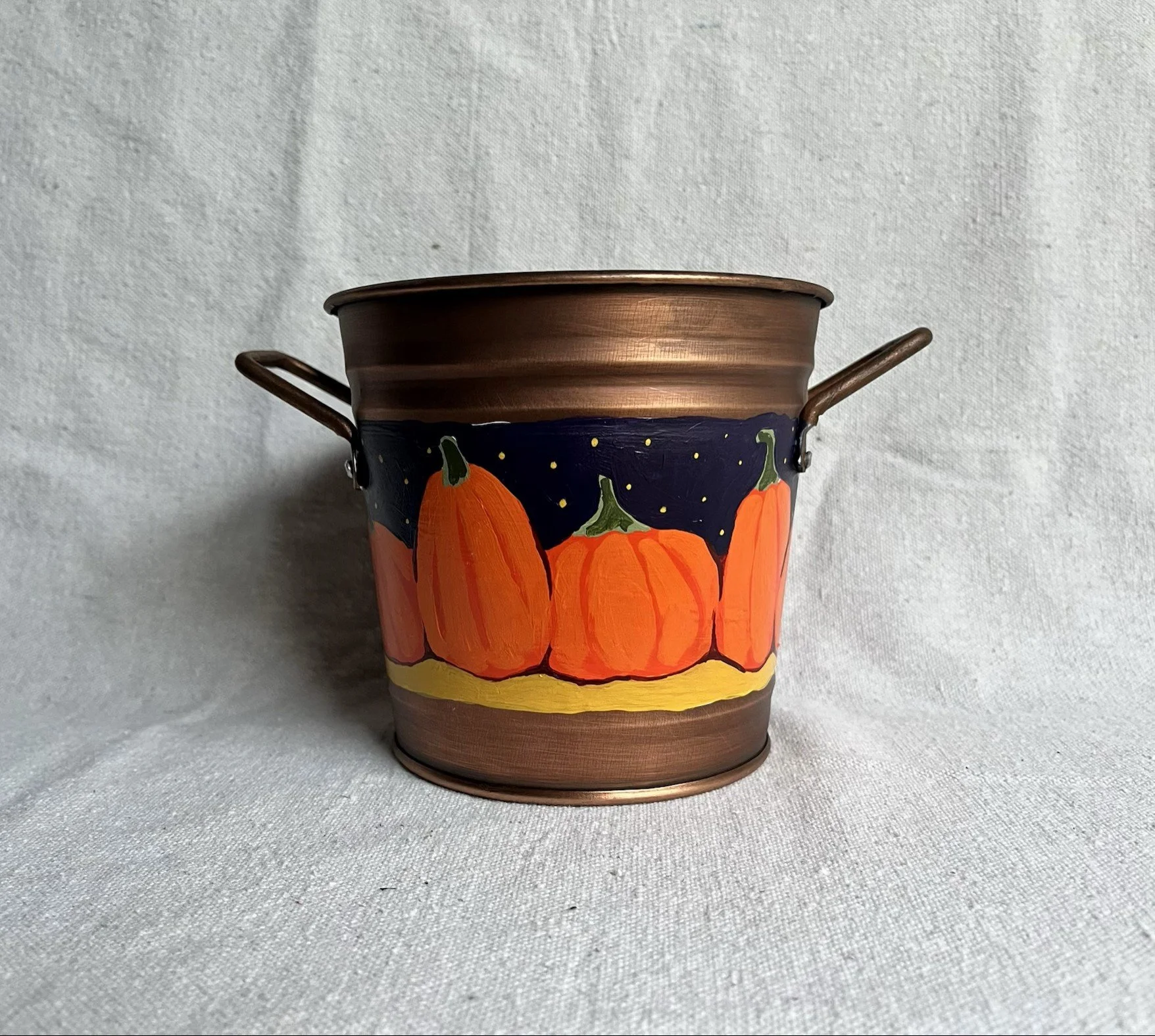 A hand painted pumpkin patch against a starry night sky, painted on a copper color tin bucket.