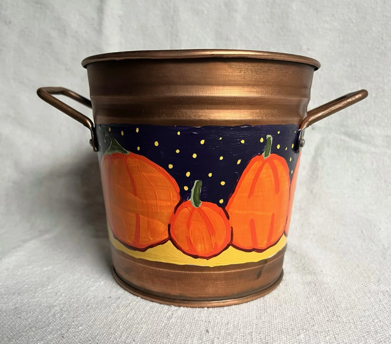 d A hand painted pumpkin patch against a starry night sky, painted on a copper color tin bucket.