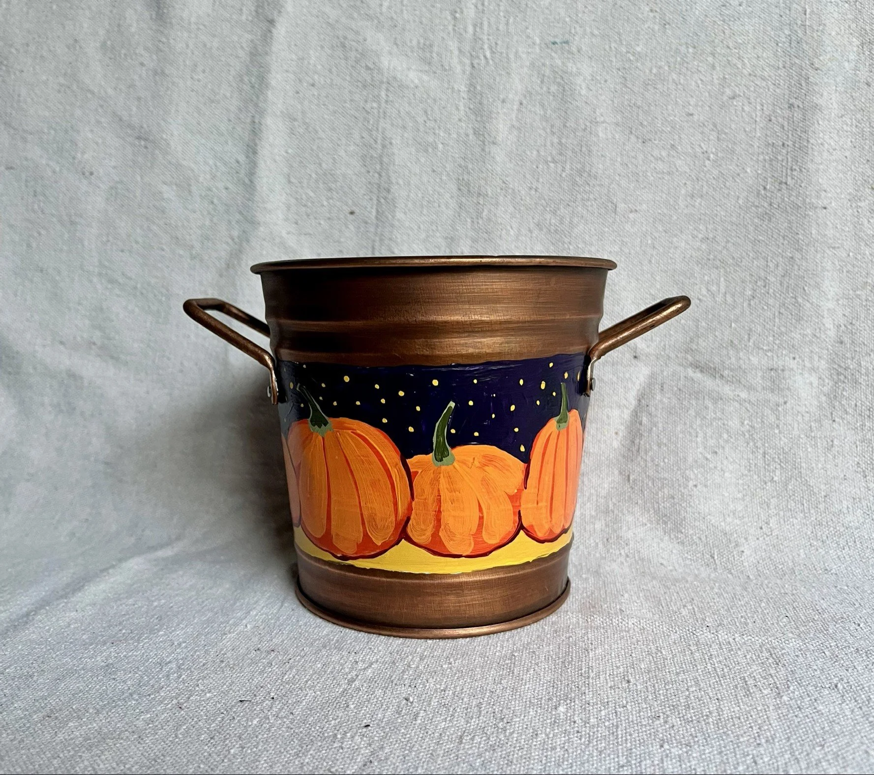 A hand painted pumpkin patch against a starry night sky, painted on a copper color tin bucket.