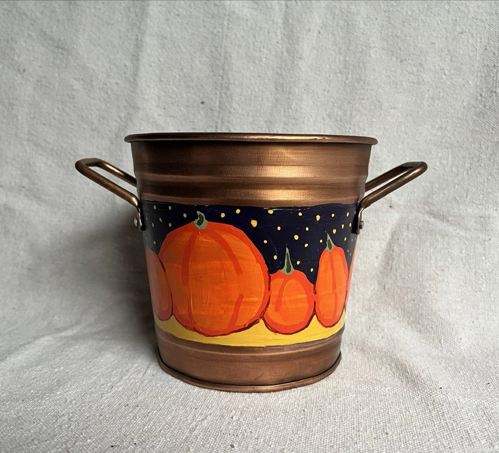 A hand painted pumpkin patch against a starry night sky, painted on a copper color tin bucket.