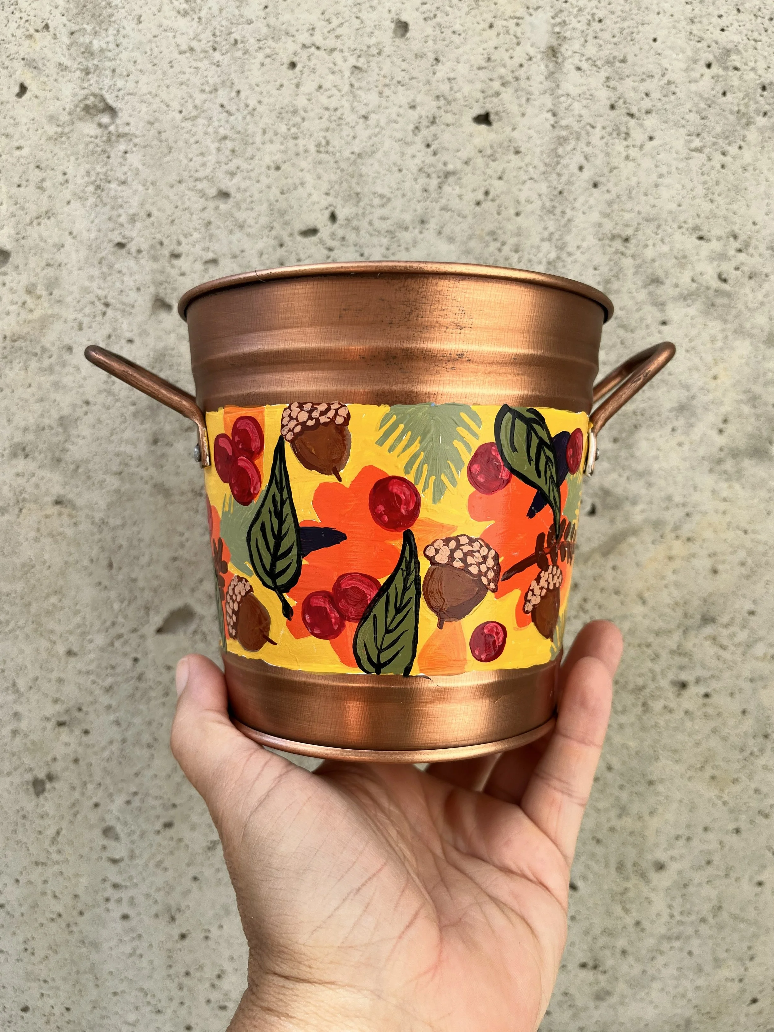 Copper color bucket hand painted with fall decorations like acorns and leaves