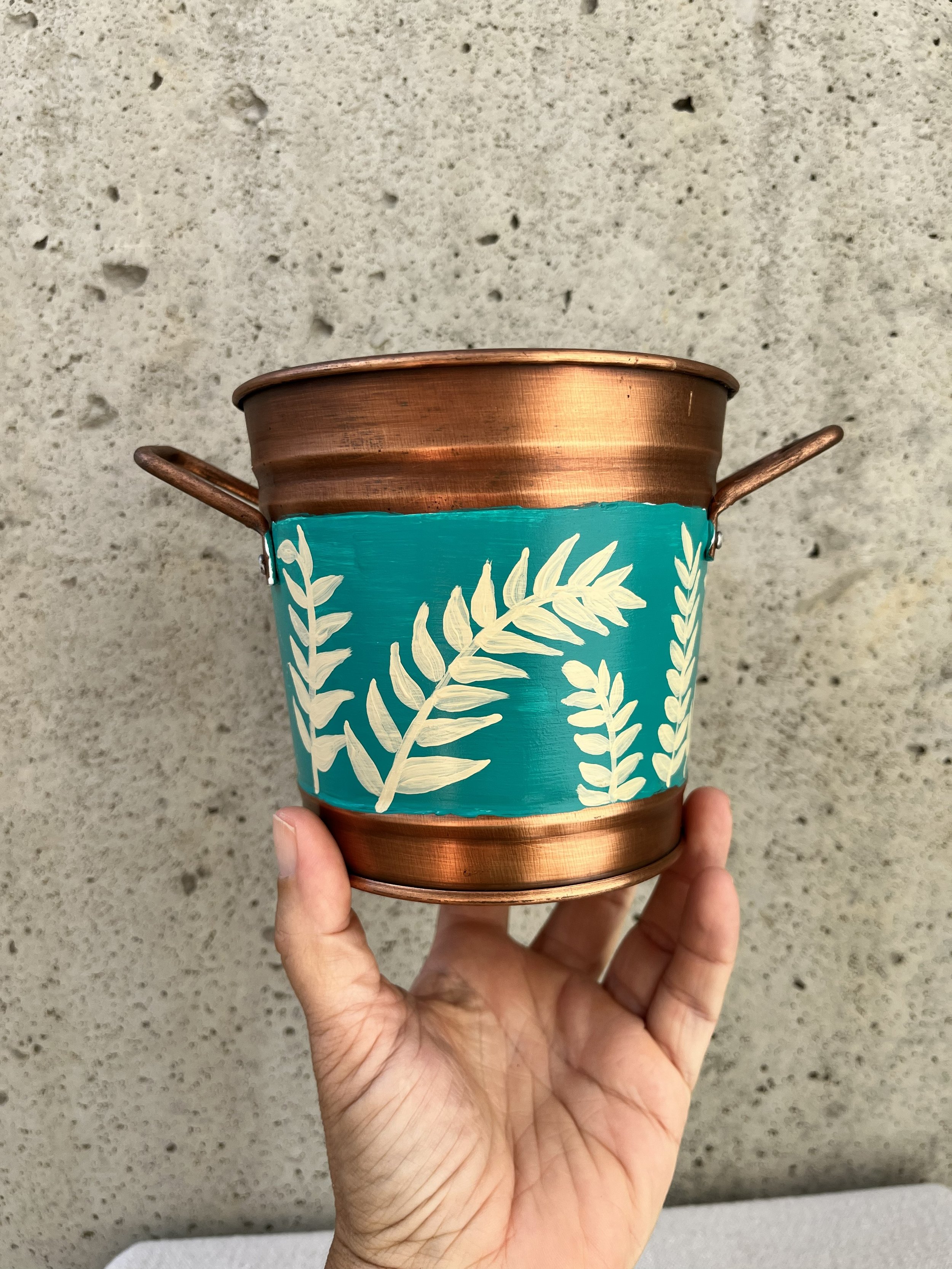 Hand painted frond of leaves on a blue background. Copper color bucket.