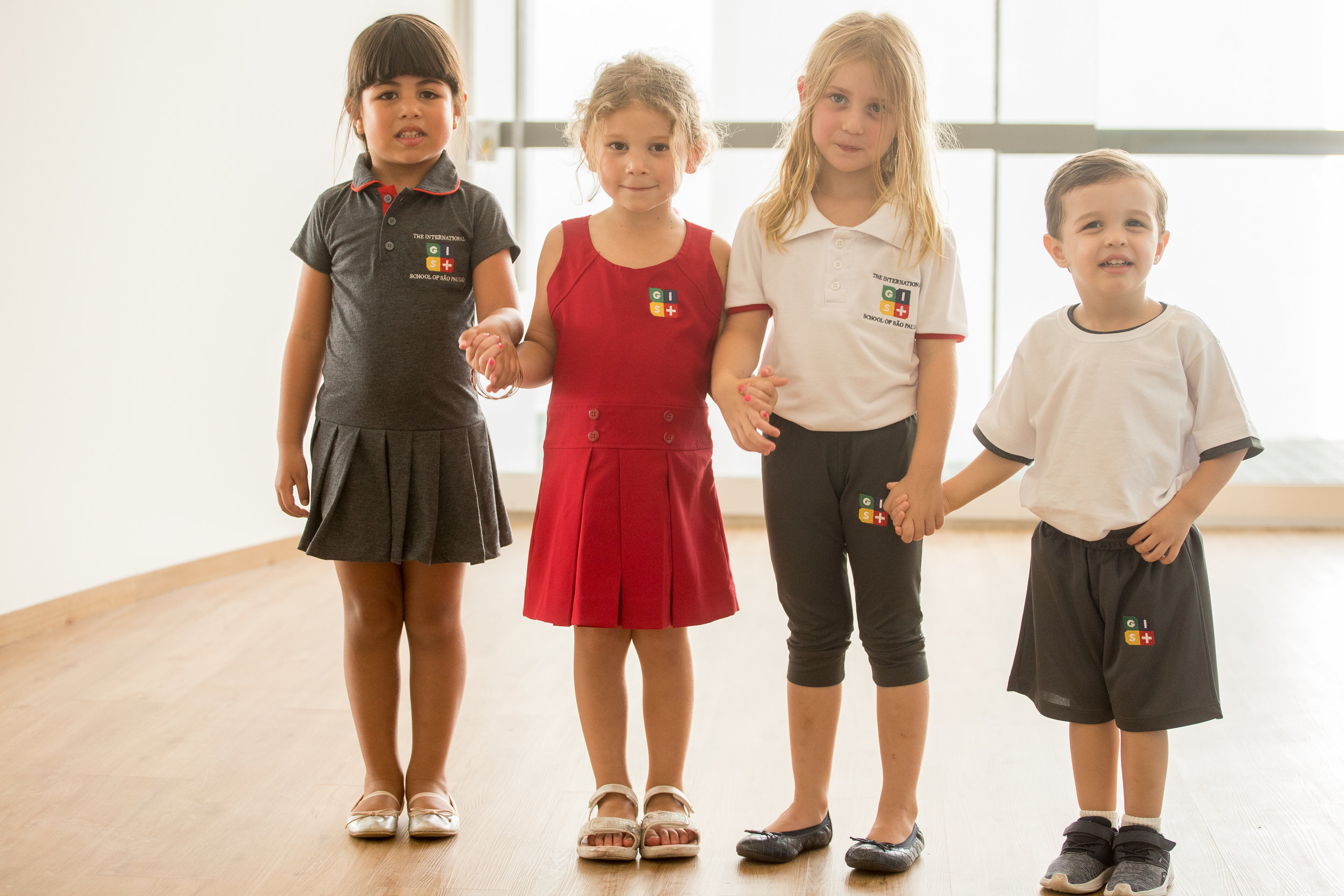 Students wear different models of the uniform: gray dress with polo collar and pleated skirt; red tank top dress; white polo shirt and gray capri pants; and white t-shirt and gray shorts.
