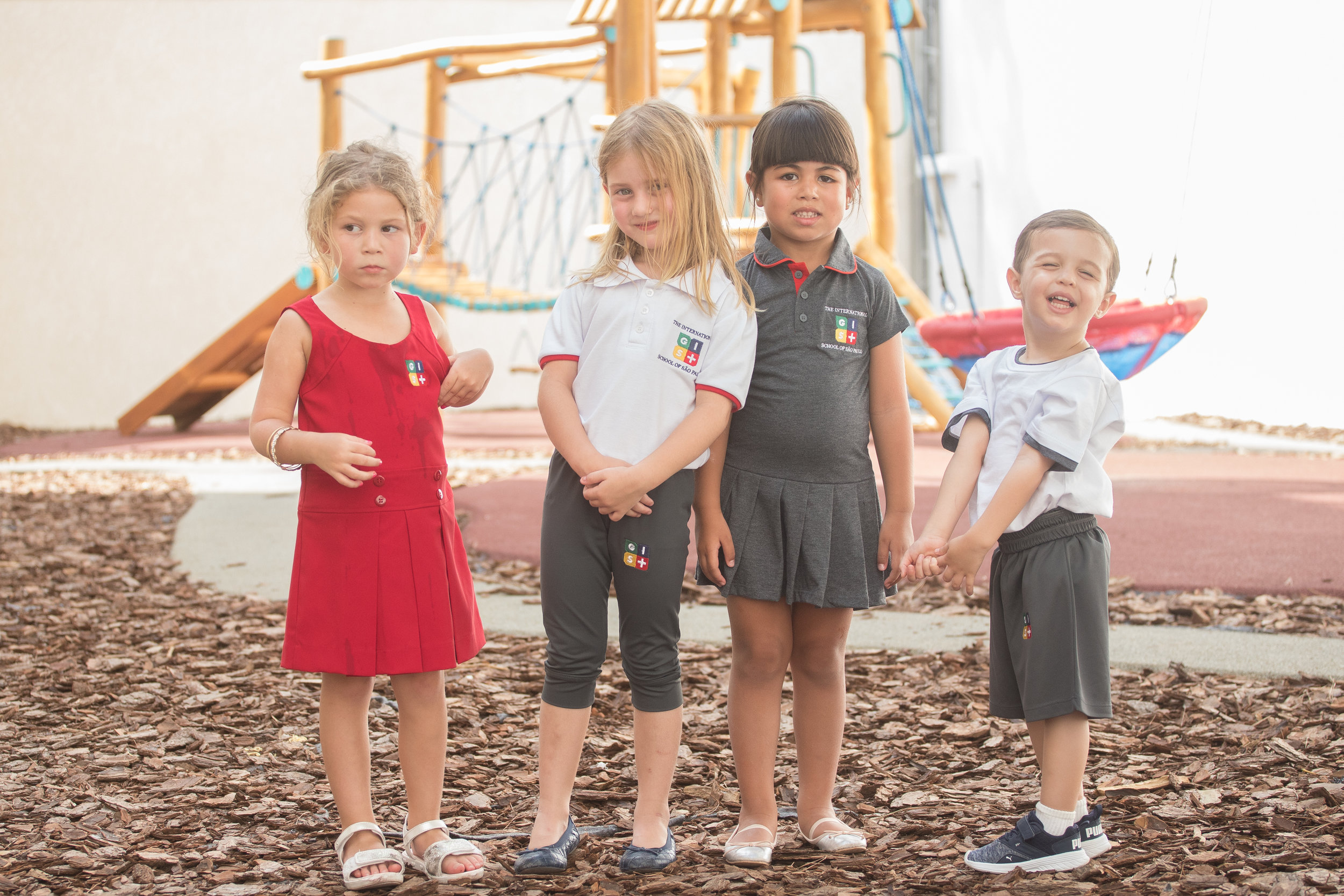 Students wear different models of the uniform: red tank top dress, white polo shirt and gray capri pants, gray polo collar dress and pleated skirt, and white shirt and gray shorts.