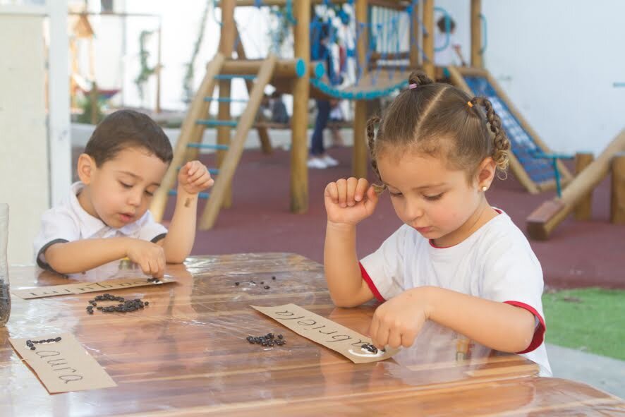 Two students perform a proposed activity in bilingual education, using glue, paper and beans.