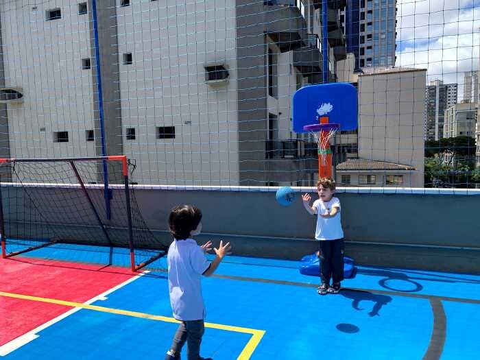 Two students in physical education activity on the sports court that is located on the top floor of the school in an open area, with reinforced nets around the structure to ensure safety.