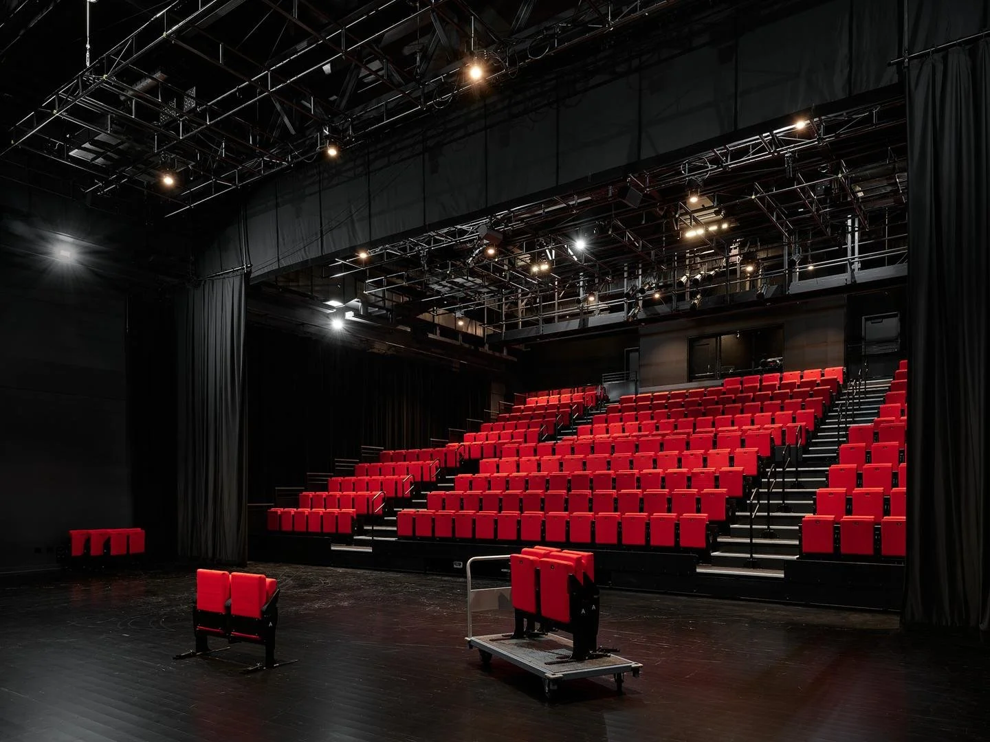  Fully lit interior of Le Grand-Espace black box theater showing the deployed red seating bank and overhead technical grids. 