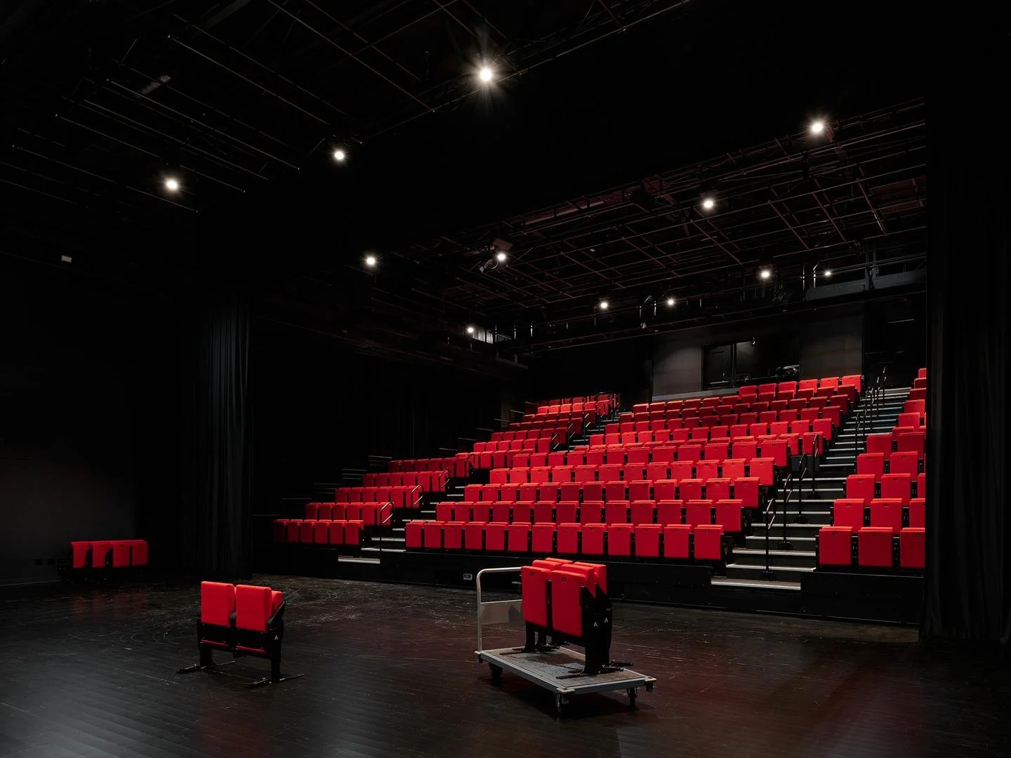  Le Grand-Espace flexible performance space shown with dim lighting, highlighting the bright red retractable seats against the dark room. 