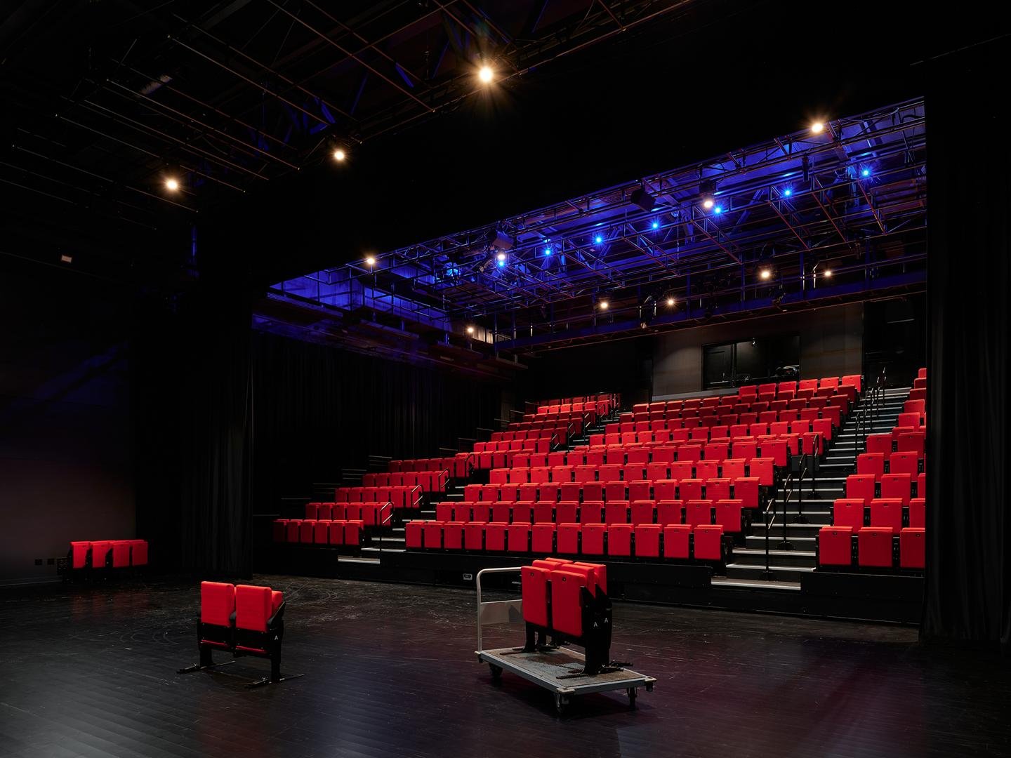 Interior of Le Grand-Espace black box theater showing the motorized red seating bank under dramatic blue stage lighting. 