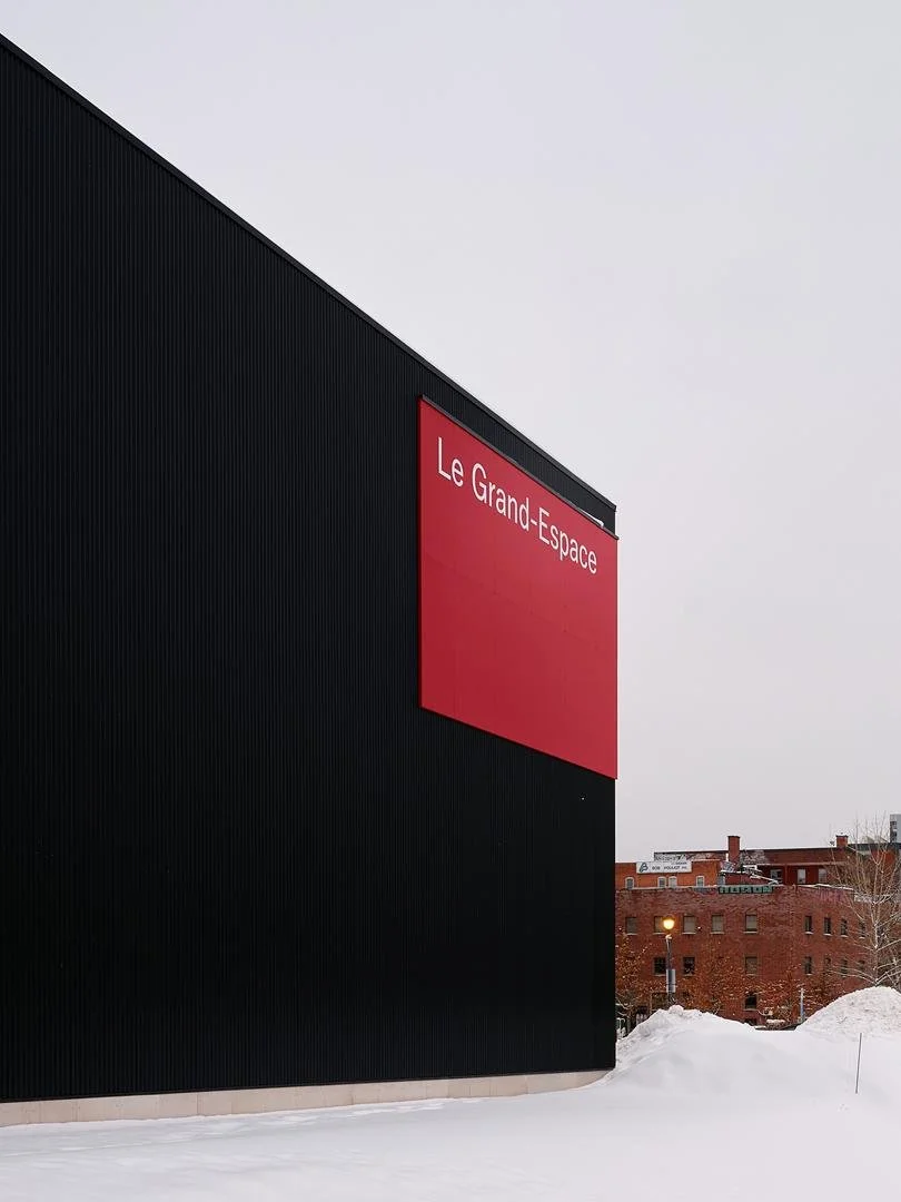 Close-up architectural detail of the bright red exterior sign panel reading "Le Grand-Espace" mounted on the dark metal cladding.