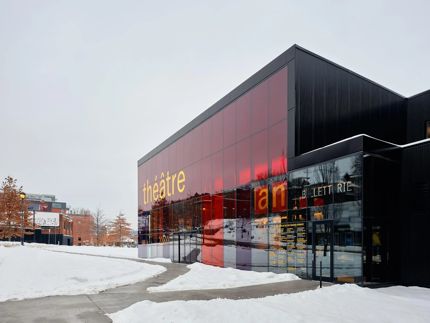 Main entrance of Le Grand-Espace, featuring the transparent glass box office framed by the building's vibrant red tinted architectural glazing.