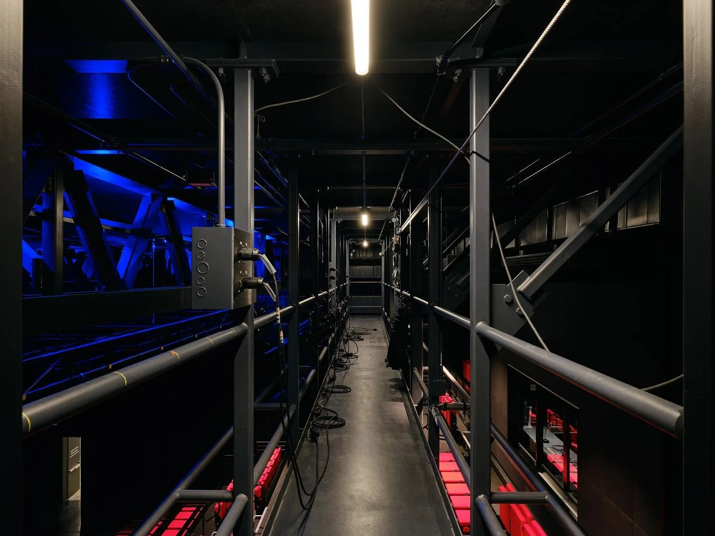 View walking along the elevated steel technical catwalk suspended above the stage in Le Grand-Espace, illuminated by linear ceiling lights.