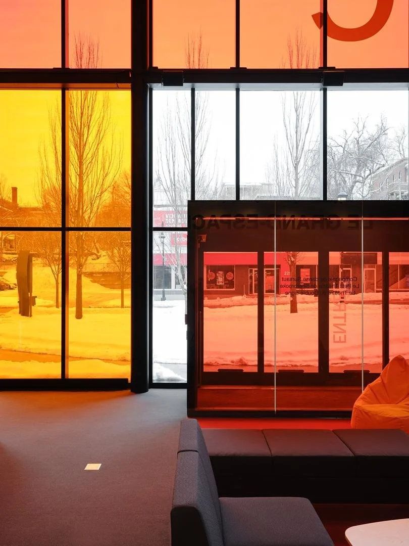 Vue depuis le foyer du Grand Espace vers l'extérieur enneigé, à travers le grand vitrage coloré en teintes orangées de la façade et du vestibule d'entrée..