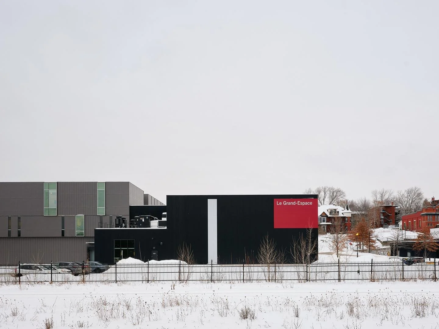 Wide landscape view of the monolithic black volume of Le Grand-Espace, punctuated by a bold red signage panel overlooking the city.
