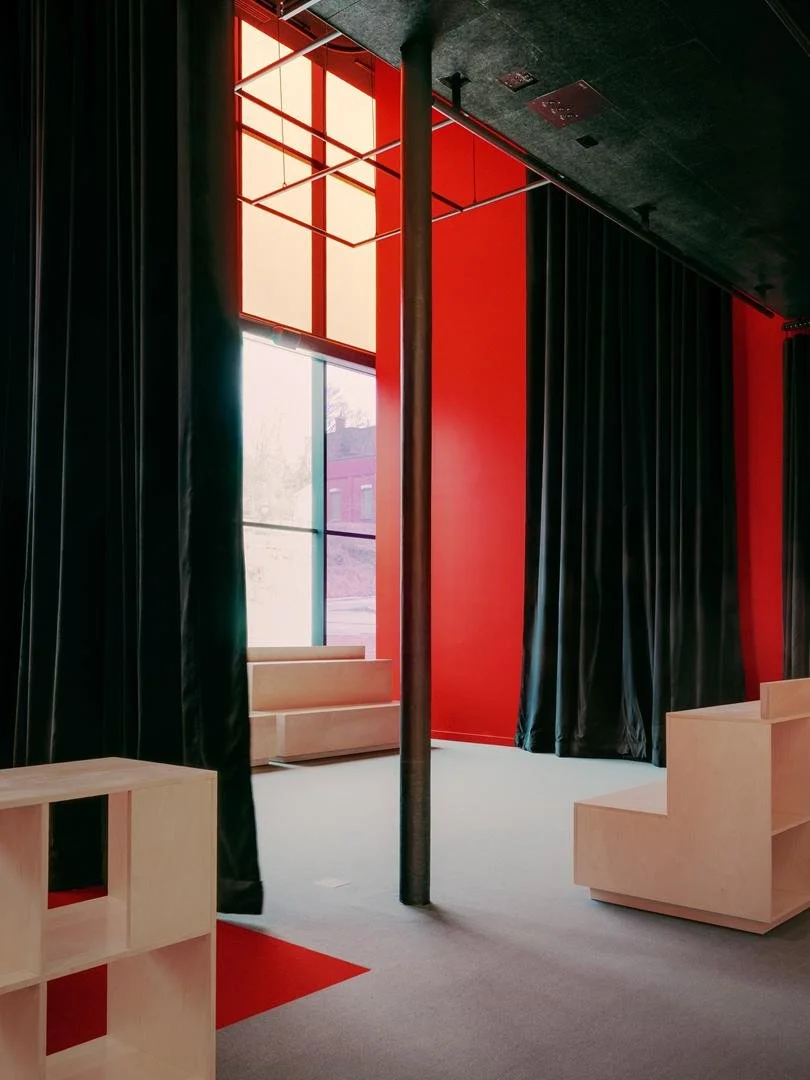 Foyer interior showing heavy black acoustic curtains drawn open to reveal red walls and natural light filtering through tinted glass.