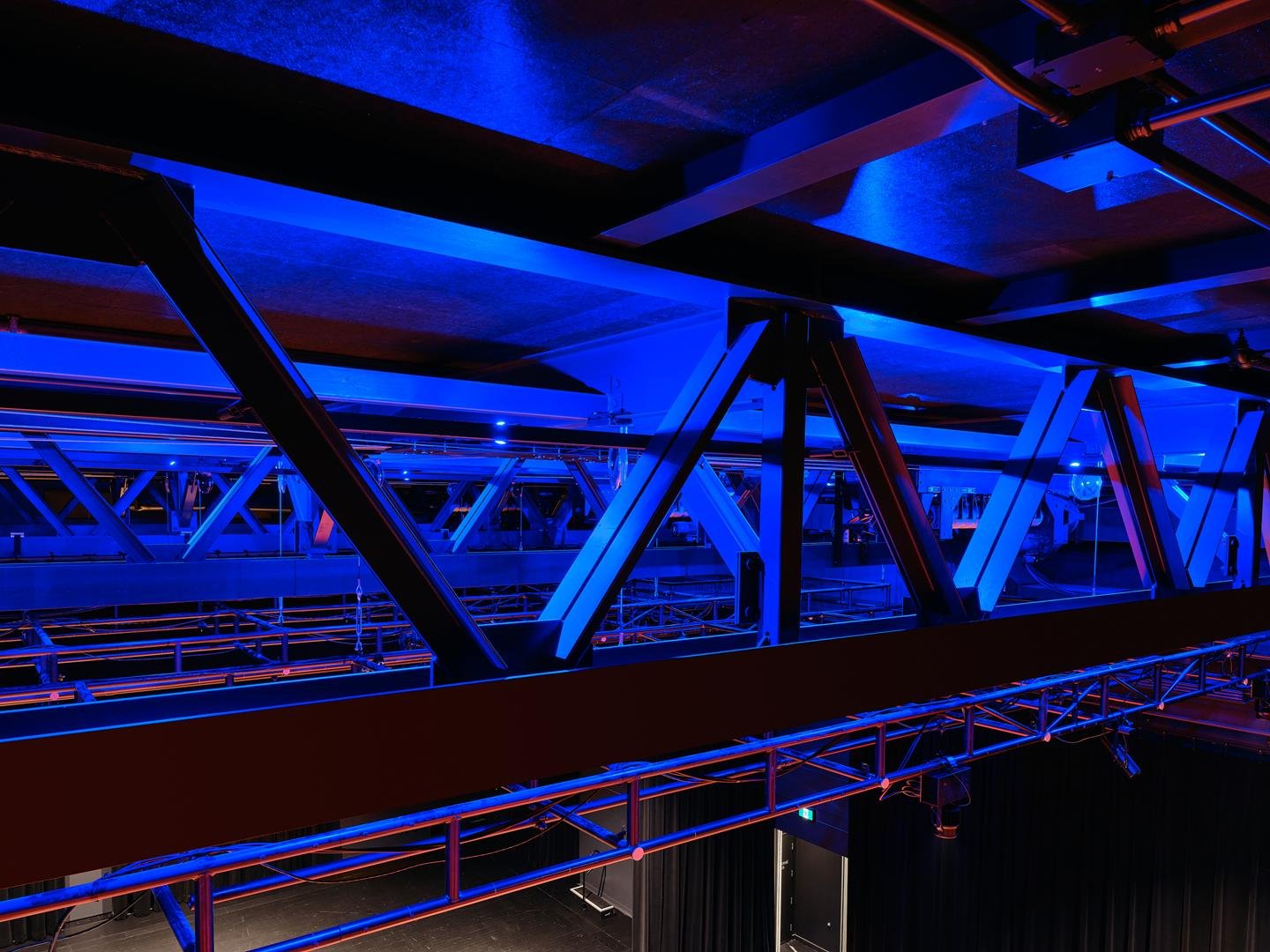 Vue des fermes d'acier de structure au plafond de la salle du Grand Espace pour supporter les équipements scénographiques sous un éclairage scénique bleu.